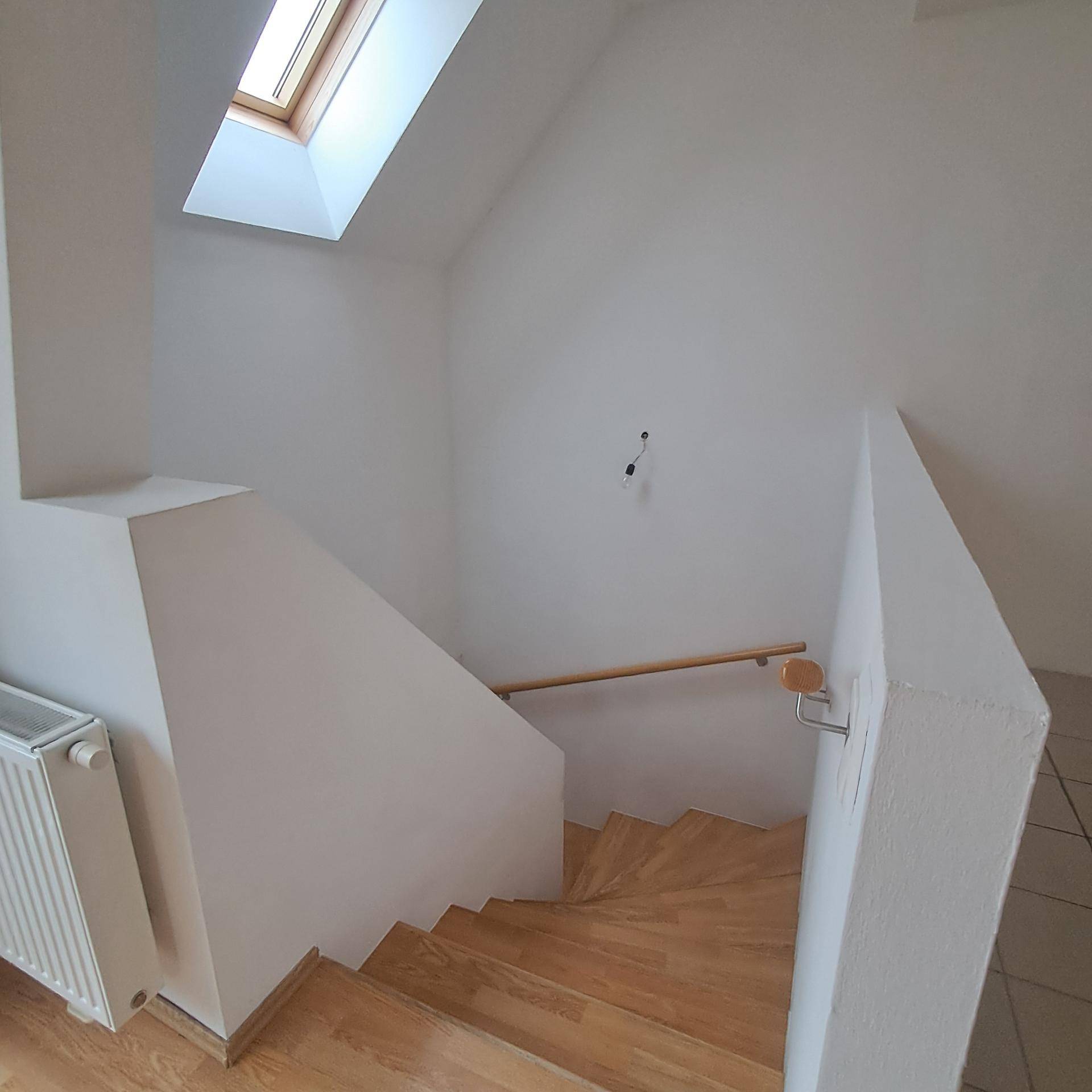 Treppenaufgang mit Holzstufen, weiß gestrichenen Wänden und einem Dachfenster für natürliches Licht.