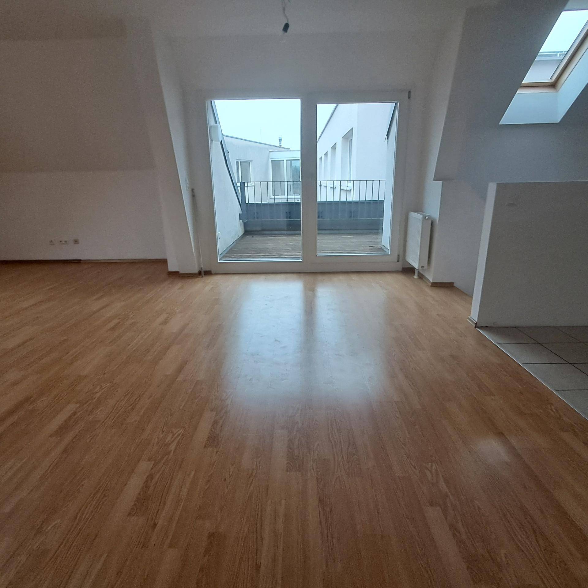 Geräumiges Wohnzimmer mit Laminatboden, Zugang zur Terrasse und einem Dachfenster.