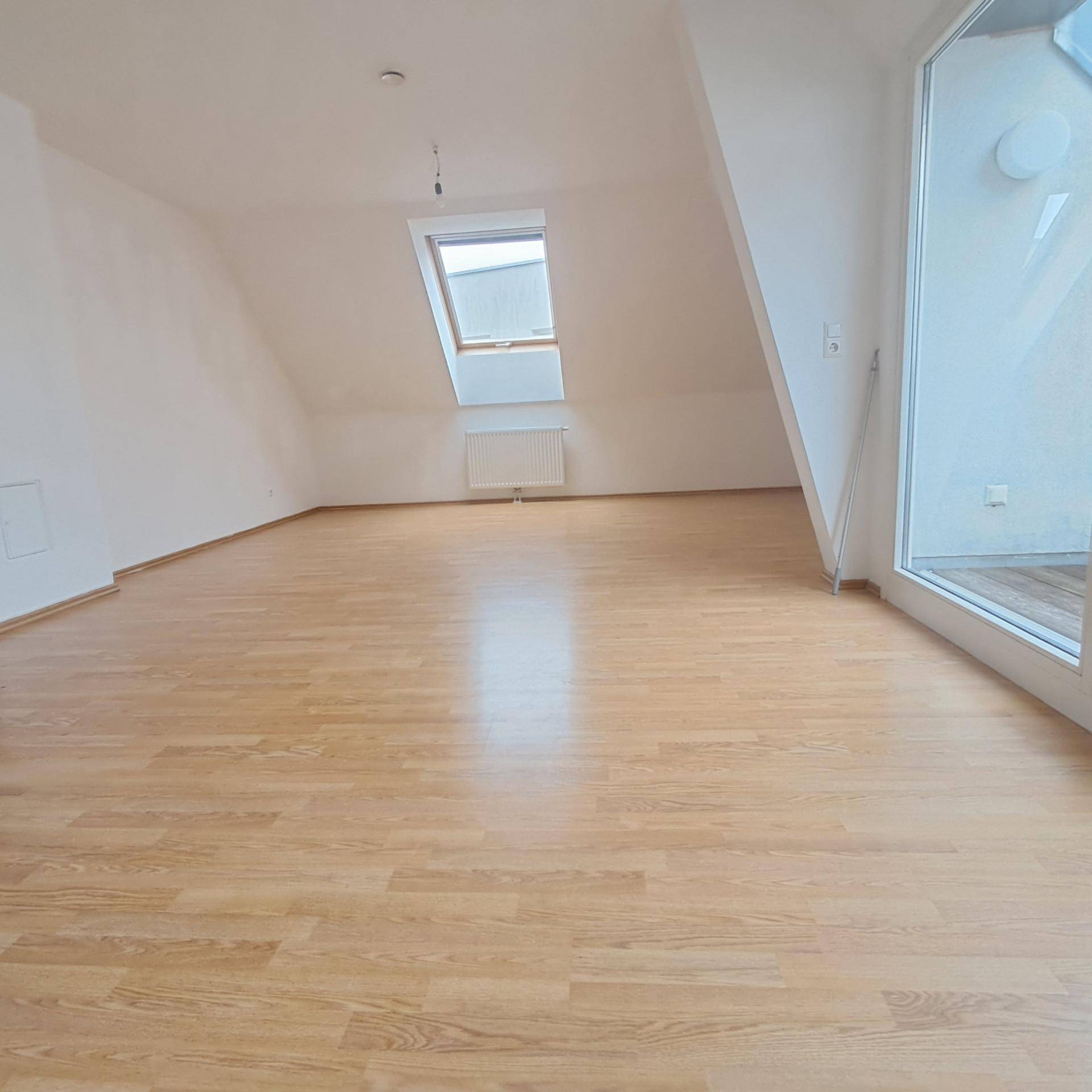 Helles Wohnzimmer im Dachgeschoss mit Laminatboden, Dachfenster und Zugang zu einem Außenbereich.
