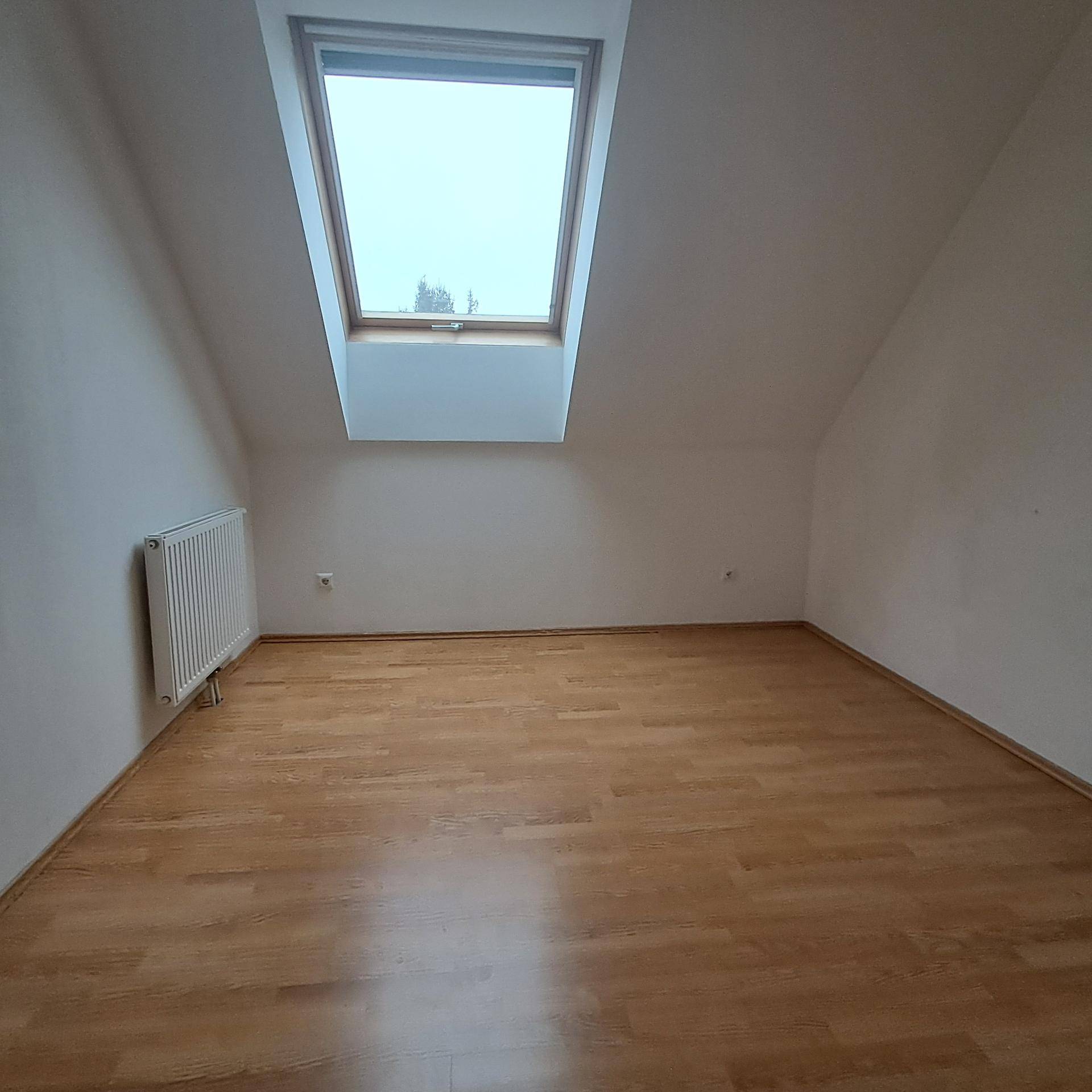 Helles Schlafzimmer im Dachgeschoss mit Laminatboden, weiß gestrichenen Wänden und Dachfenster.