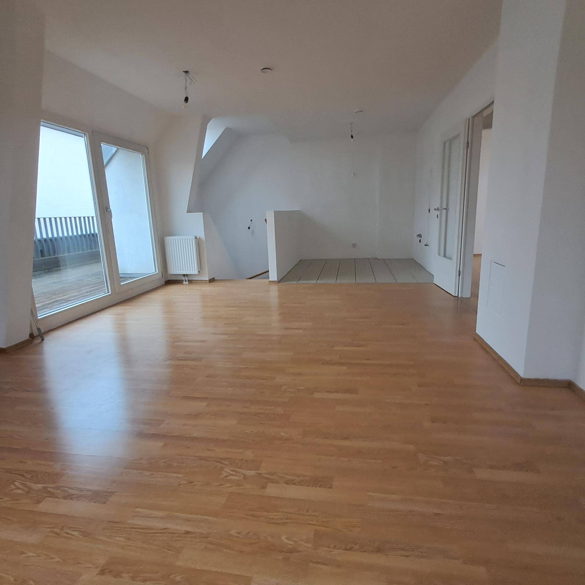 Offener Wohnbereich mit Laminatboden, Fliesenbereich und direktem Zugang zur Außenterrasse.