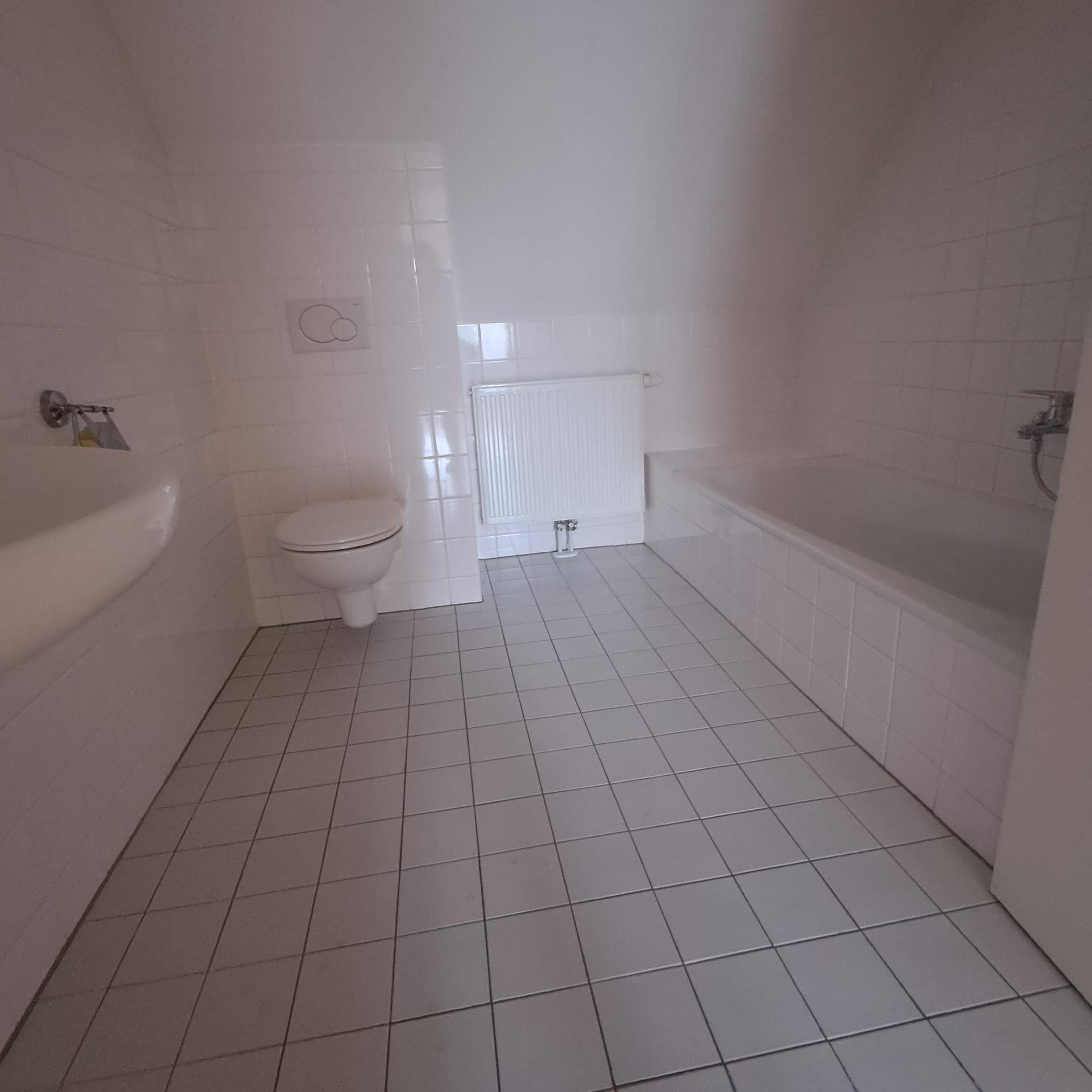 Modernes Badezimmer im Dachgeschoss mit weißen Fliesen, Badewanne, Toilette und Waschbecken.