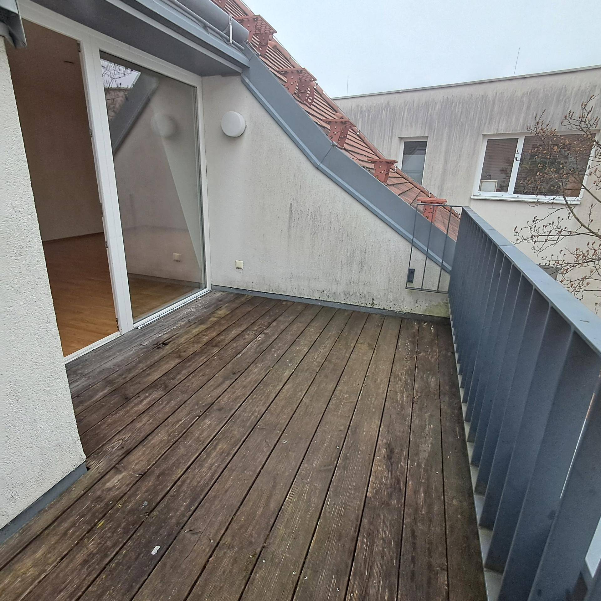 Holzterrasse mit Metallgeländer und Blick auf ein Ziegeldach, ideal für entspannte Stunden.