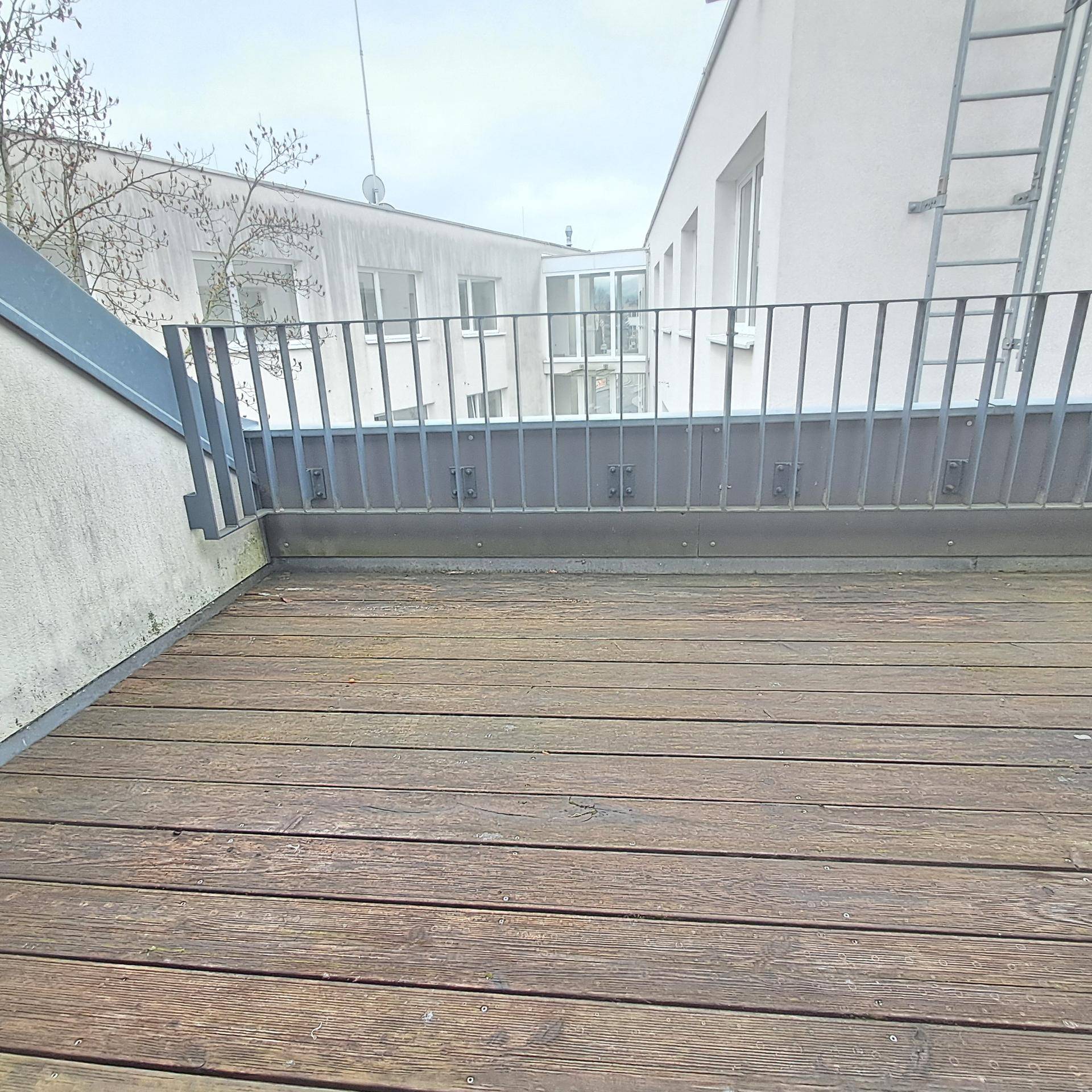 Breite Holzterrasse mit stabilem Metallgeländer, bietet Platz für Outdoor-Möbel.