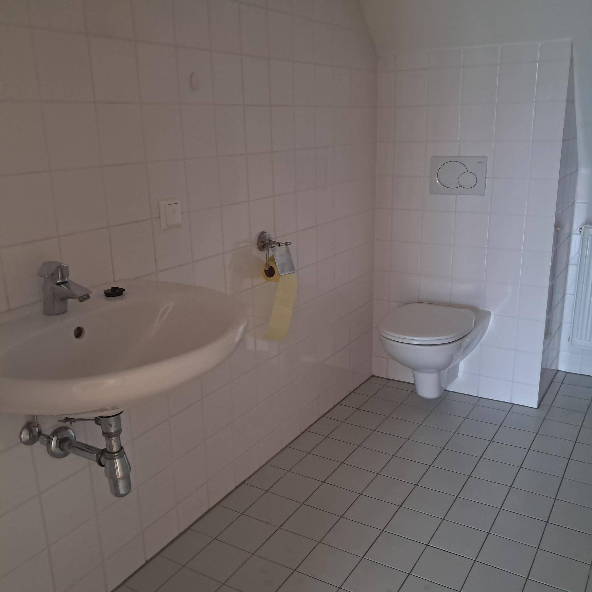 Helles Badezimmer im Dachgeschoss mit weißen Fliesen, wandhängender Toilette und Waschbecken.