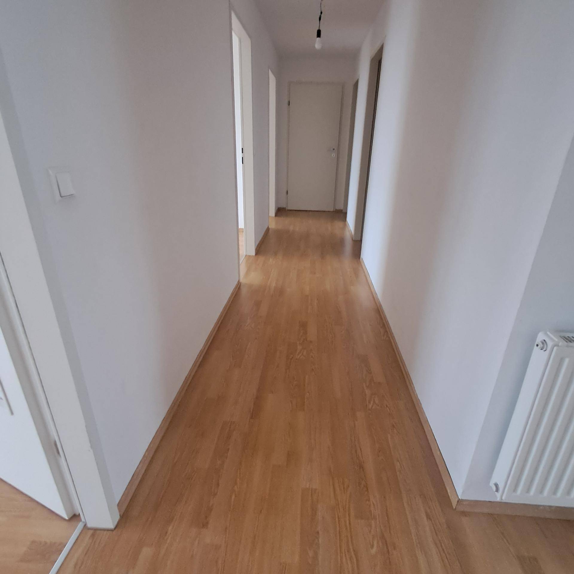 Heller Flur mit Laminatboden und weißen Wänden, der zu weiteren Räumen führt.