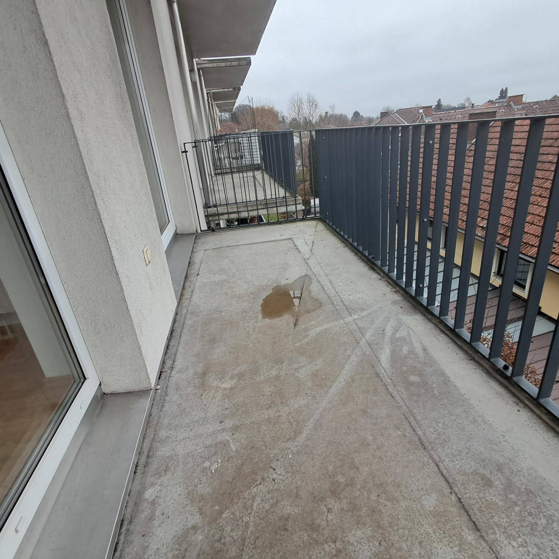 Geräumiger Balkon mit Betonboden und Metallgeländer, bietet einen Blick auf die Umgebung.