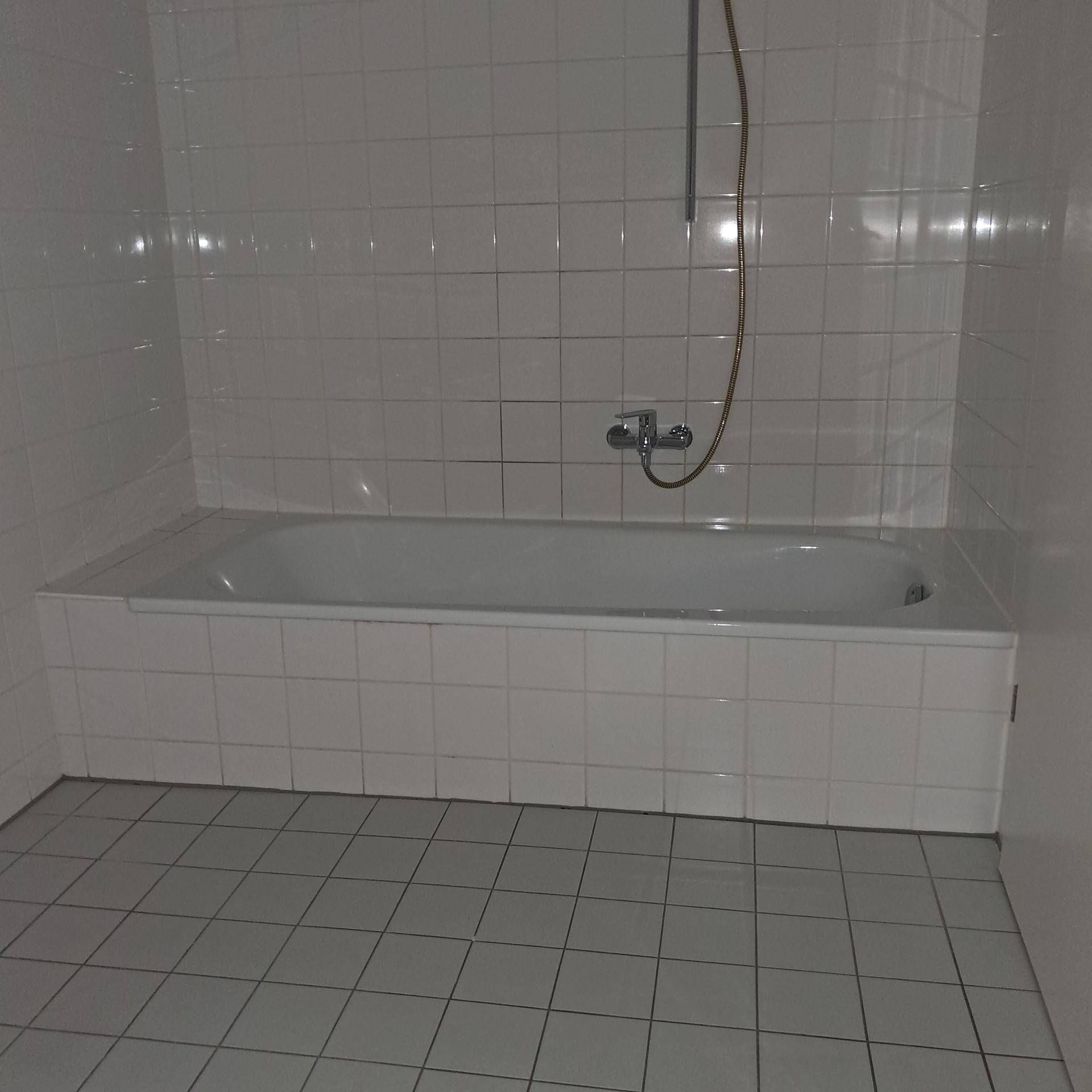 Badezimmer mit weißen Fliesen und einer eingebauten Badewanne.