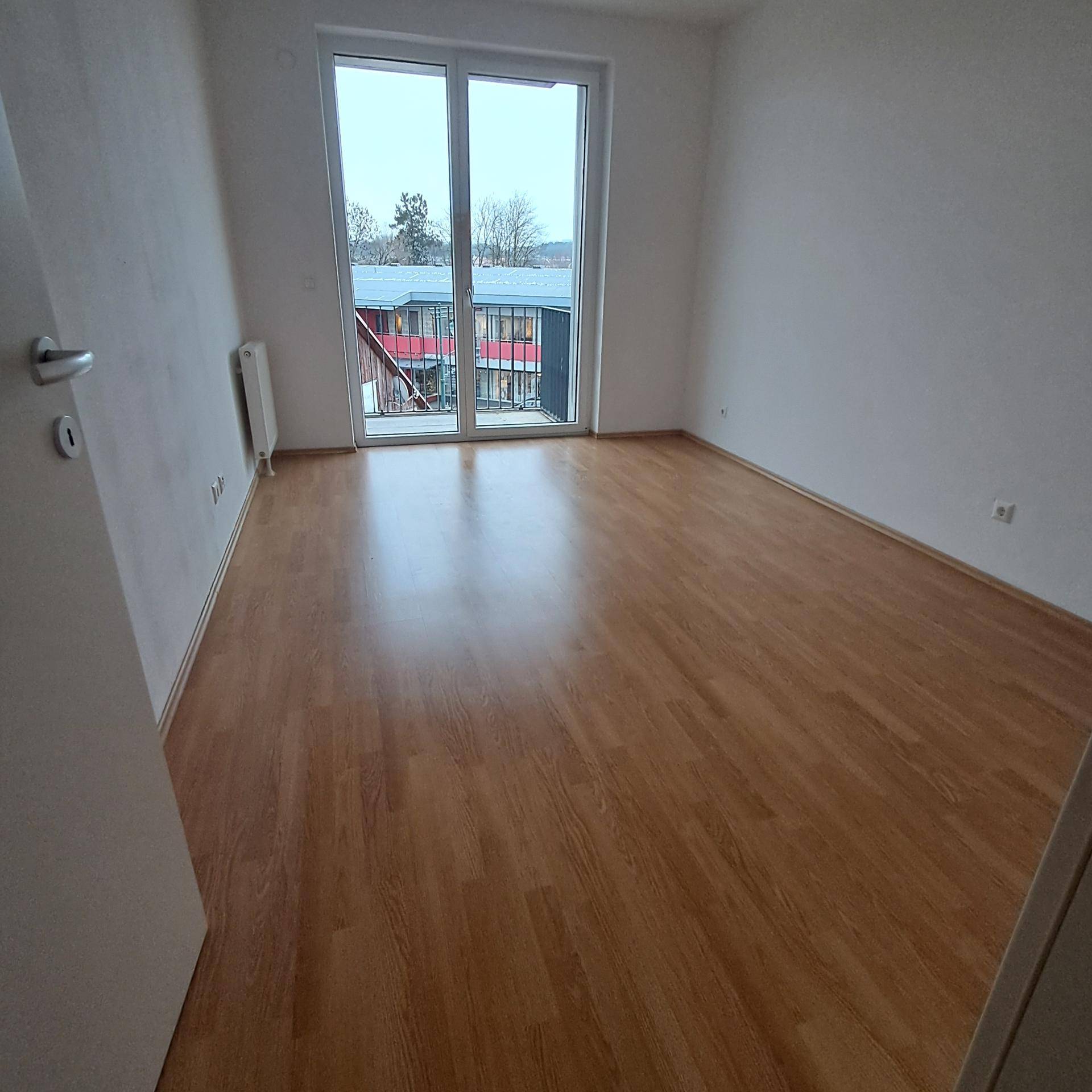 Schlafzimmer mit Laminatboden und großen Fenstern, die viel Tageslicht hereinlassen.