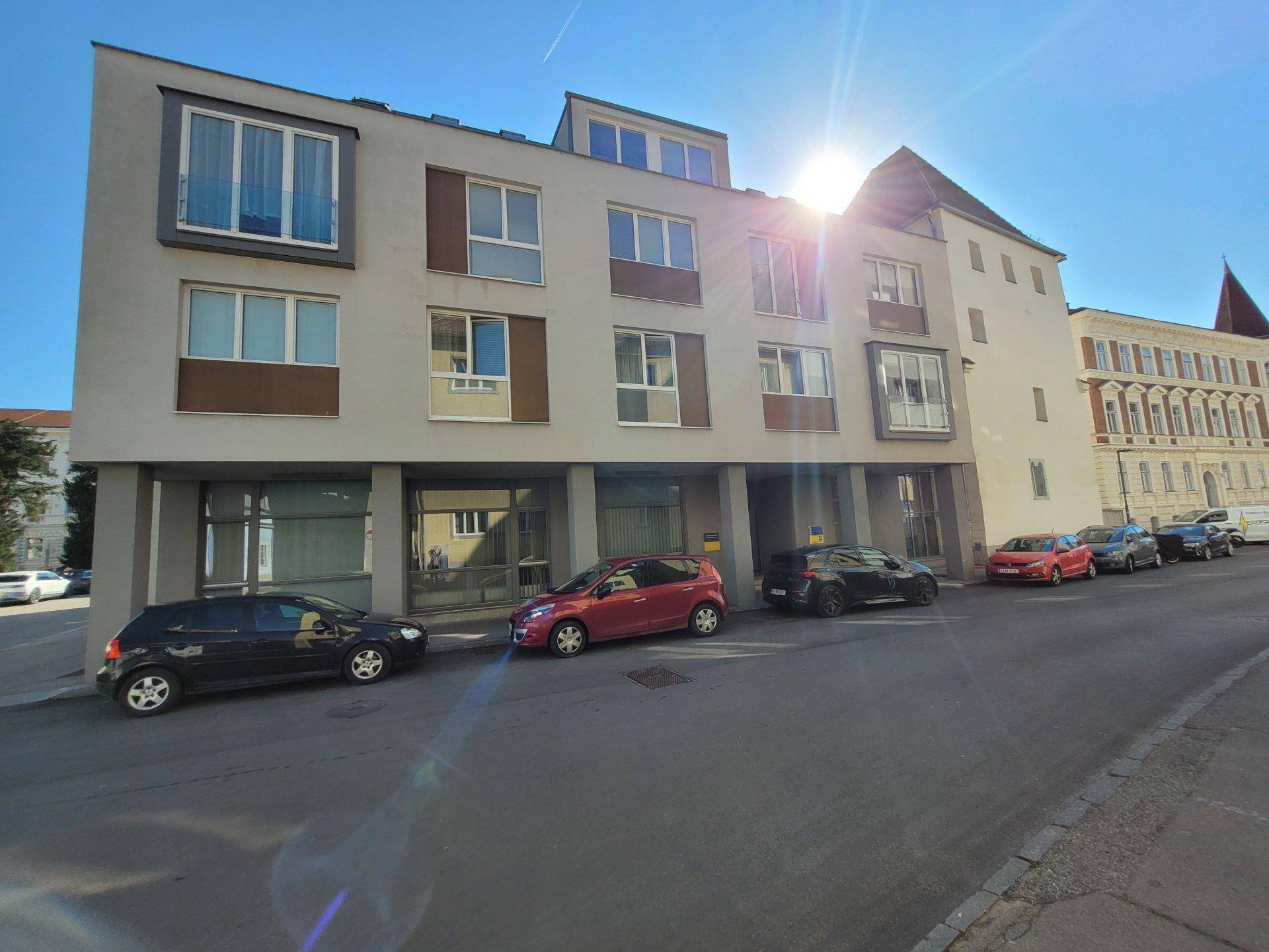 Moderne Gebäudefassade mit großen Fenstern und parkenden Autos an der Straße.