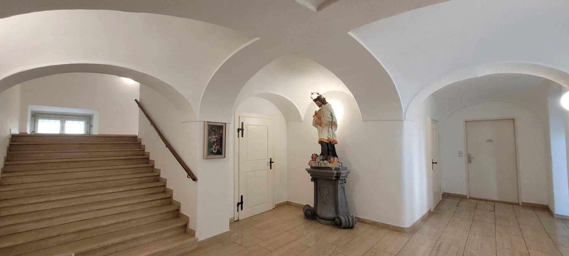 Geräumiger Flur mit gewölbten Decken, Steinboden und einer historischen Statue.