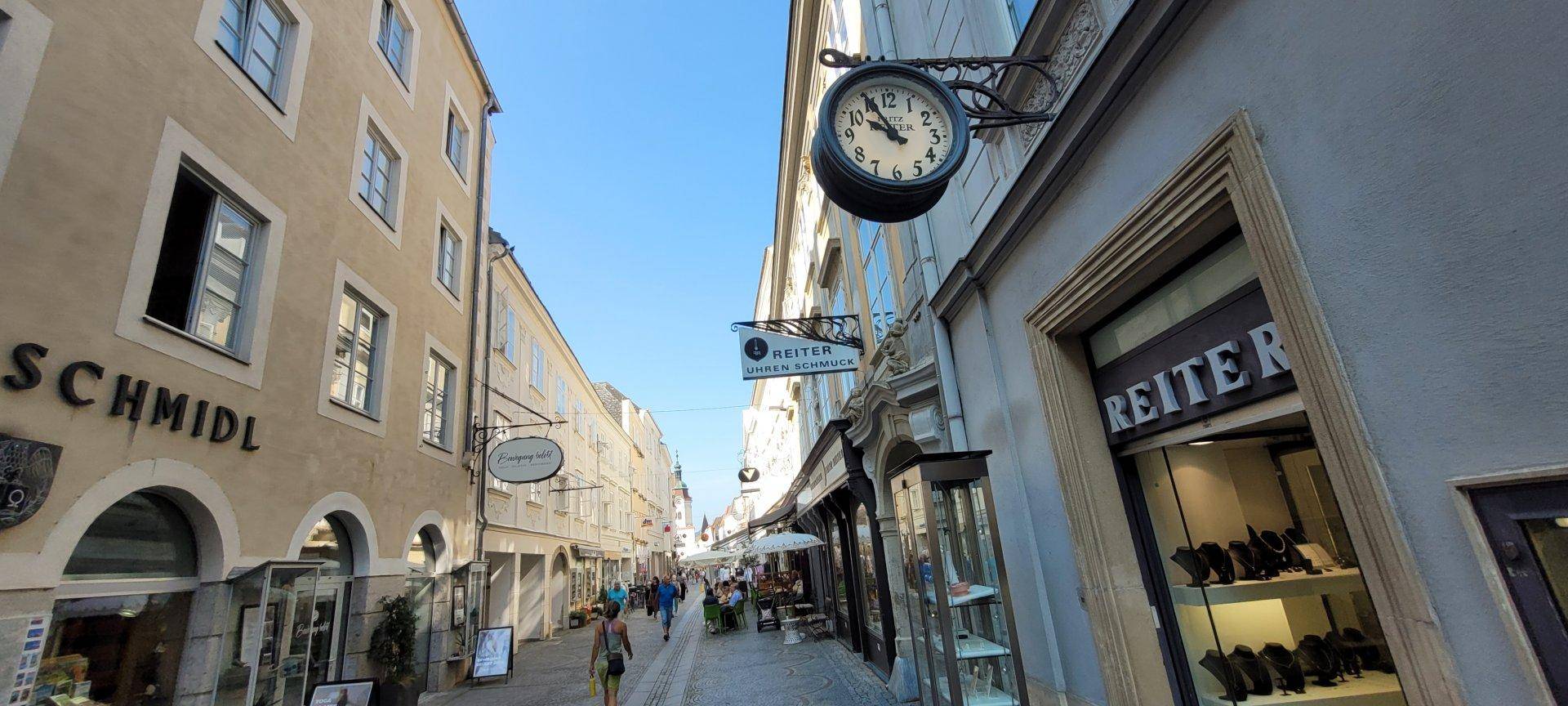 Historische Einkaufsstraße mit Geschäften, Gebäuden und einer alten Uhr an der Fassade.