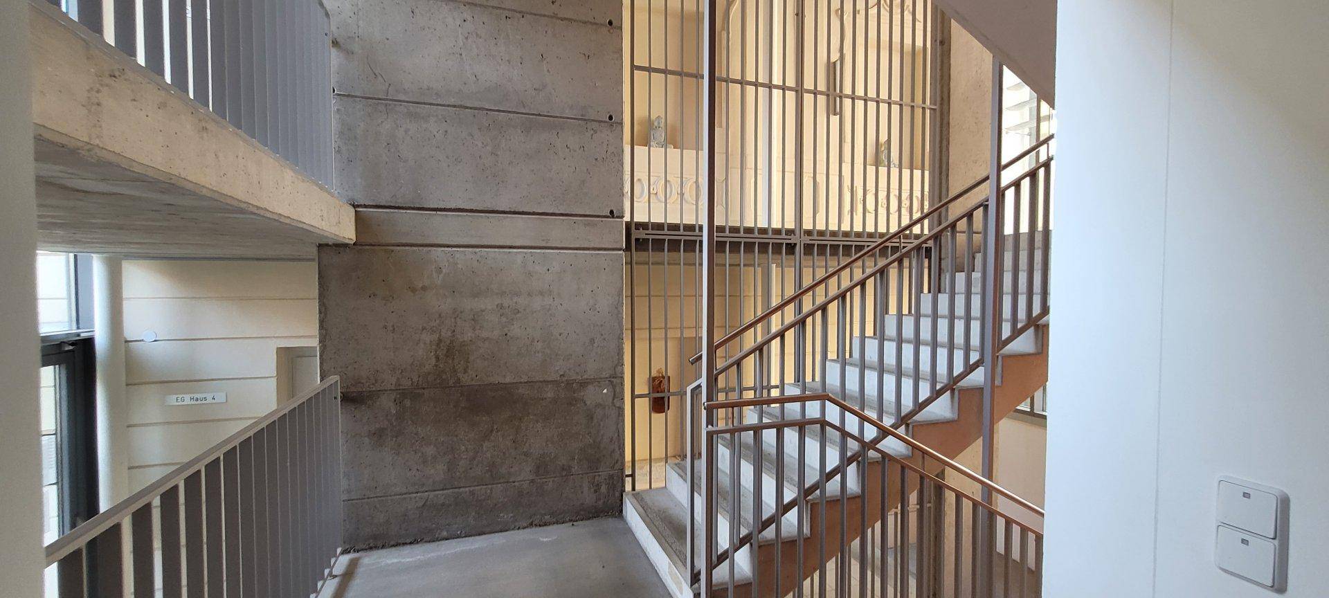 Modernes Treppenhaus mit Betonwänden und Metallgeländern, das verschiedene Etagen verbindet.