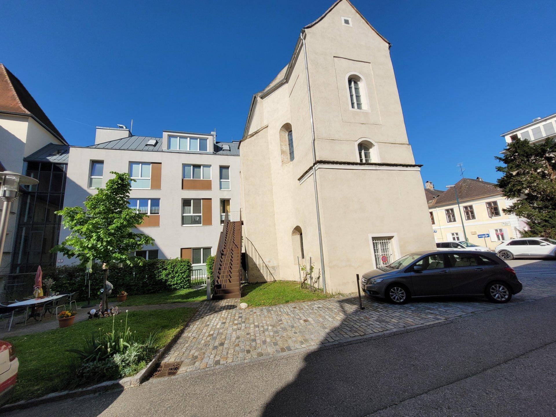 Historisches Gebäude mit markantem Turm und angrenzendem modernen Wohnhaus im Innenhof.
