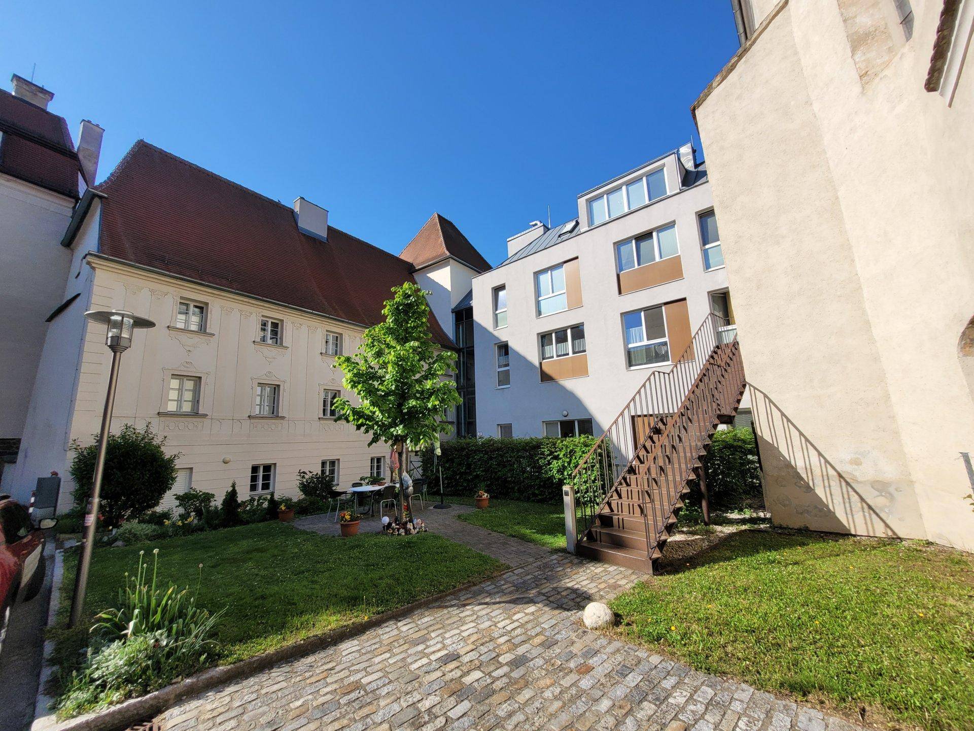 Gepflegter Innenhofgarten mit Treppe zu den oberen Etagen und Blick auf die umliegenden Gebäude.