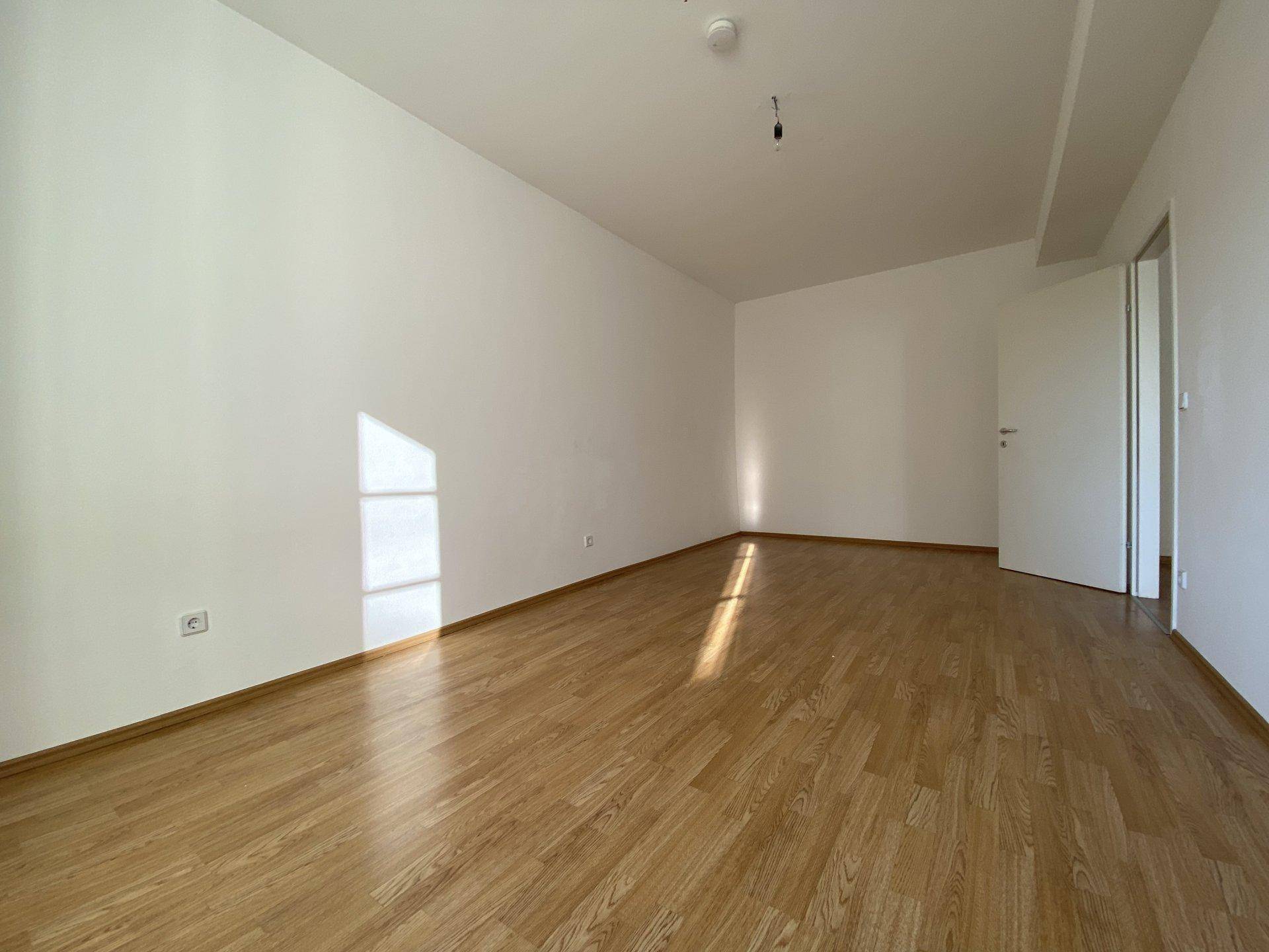 Leerer Raum mit hellem Holzfußboden und weißen Wänden, bereit zur individuellen Gestaltung.