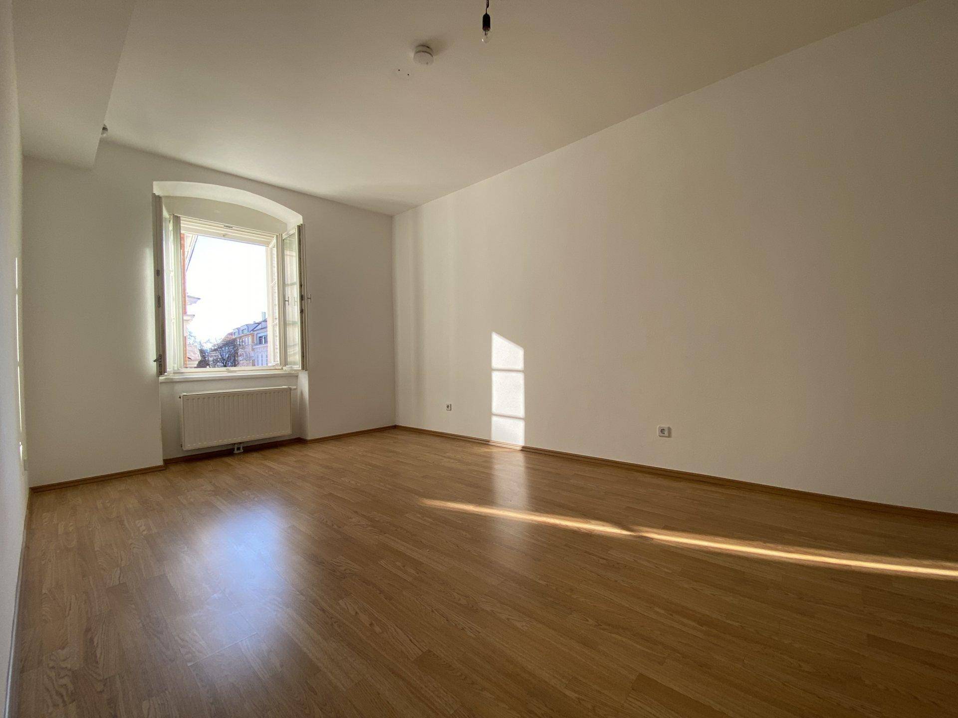 Heller Raum mit Holzfußboden und einem Fenster, das viel Tageslicht hereinlässt.