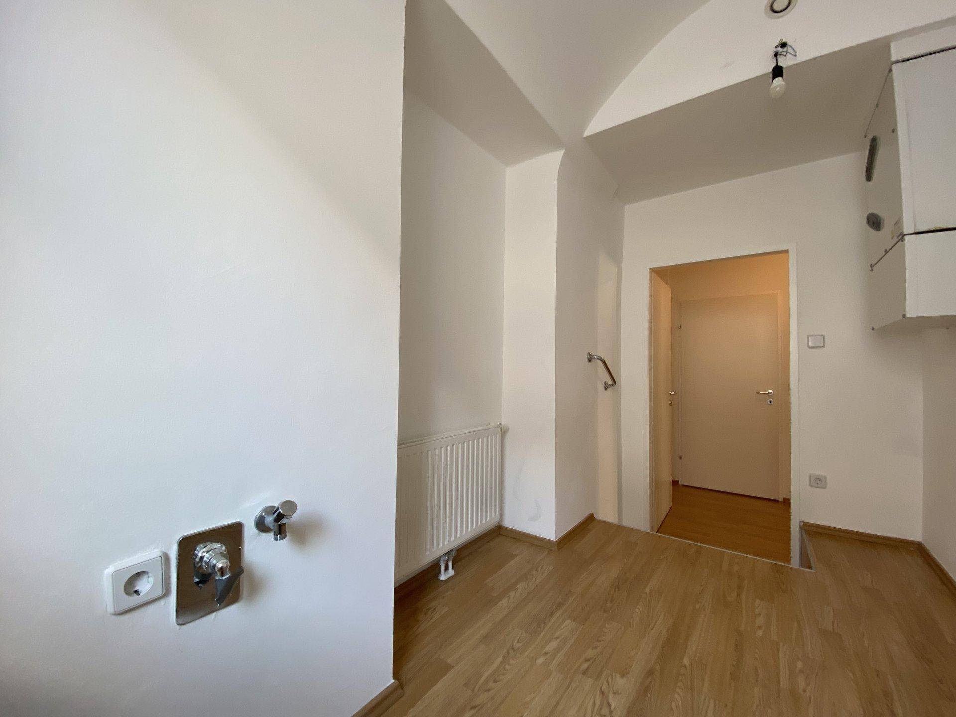 Funktionaler Raum mit Anschlüssen für Geräte, Heizkörper und Holzfußboden.