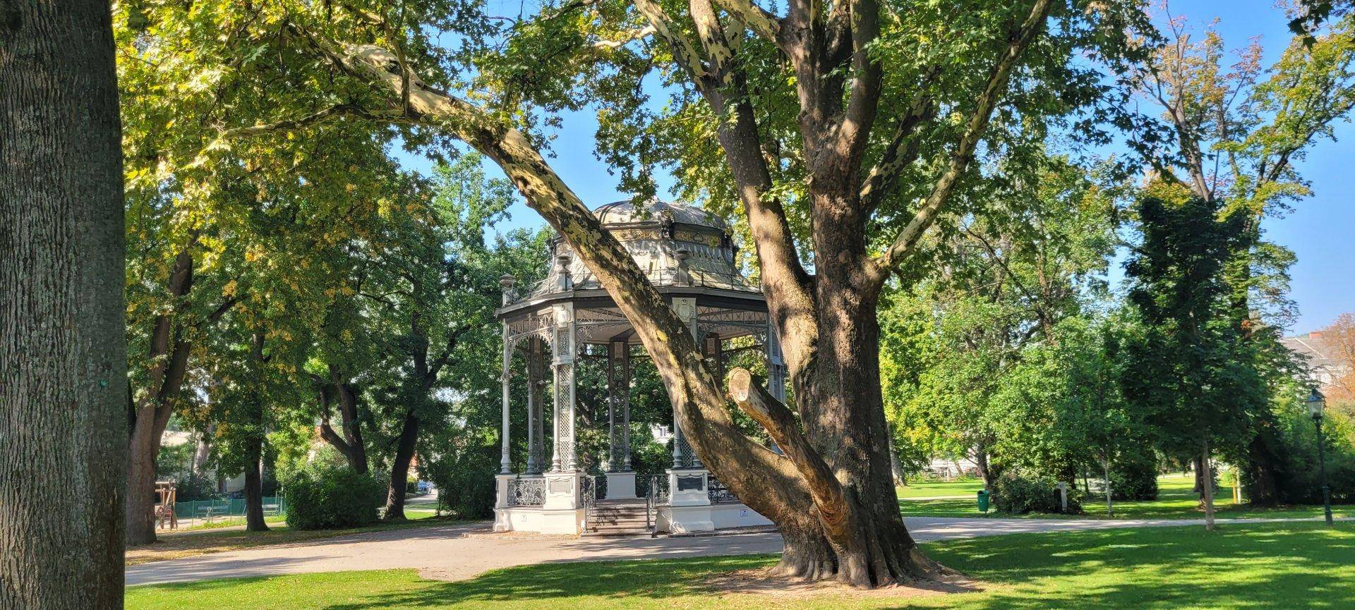 Malerischer Park mit einem historischen Pavillon und großen, alten Bäumen.