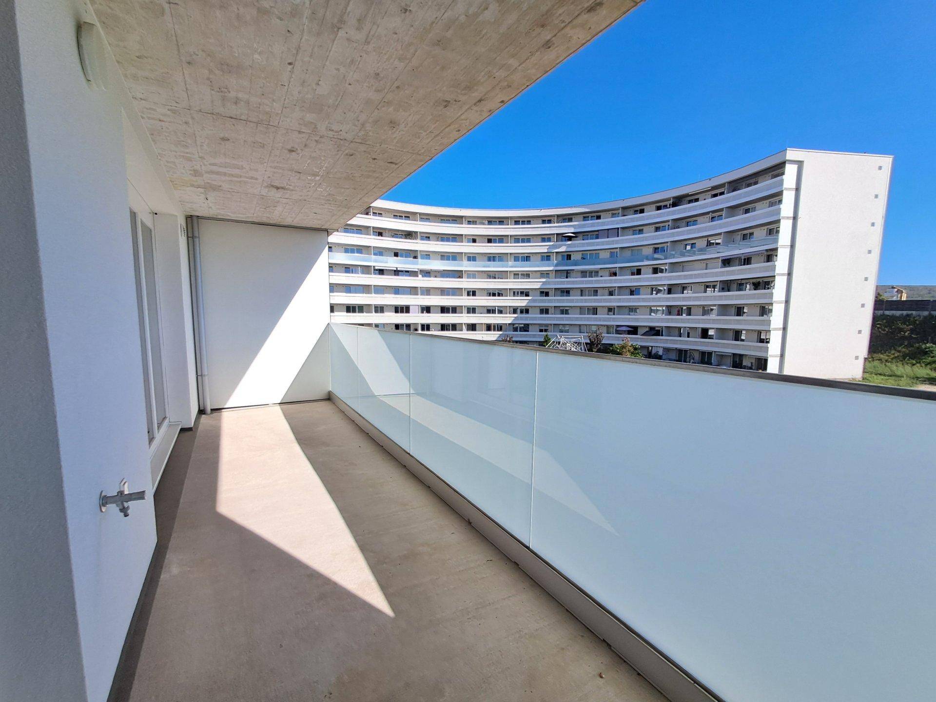 Geräumiger Balkon mit Blick auf ein gegenüberliegendes Gebäude und klarem Himmel.