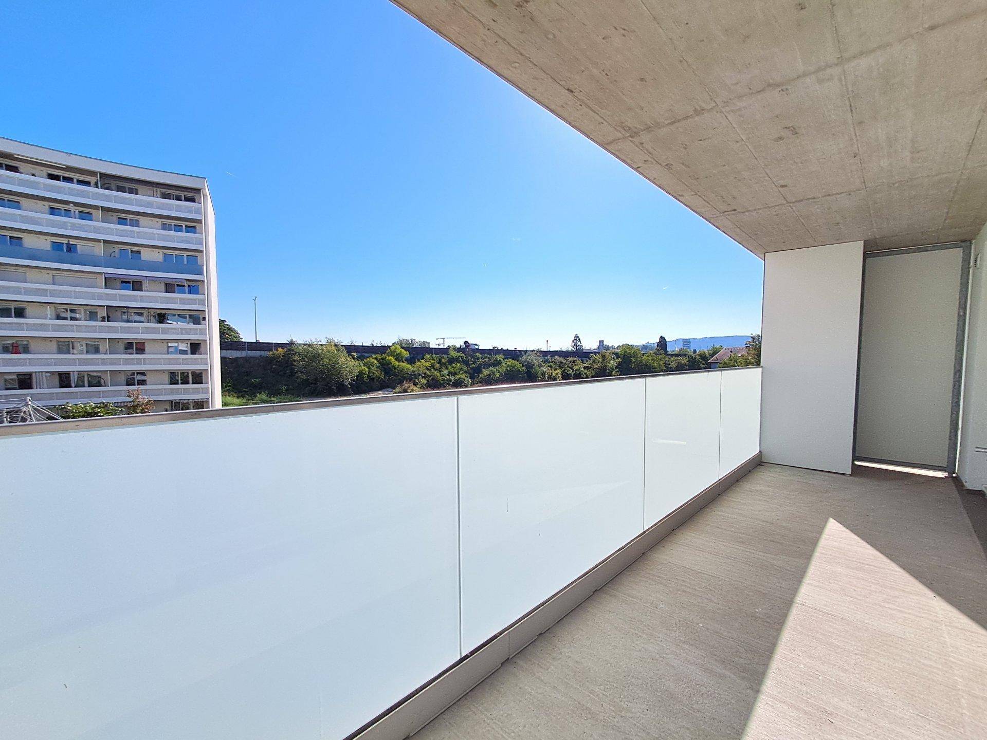 Heller Balkon mit moderner Glasbrüstung und weitem Blick unter blauem Himmel.
