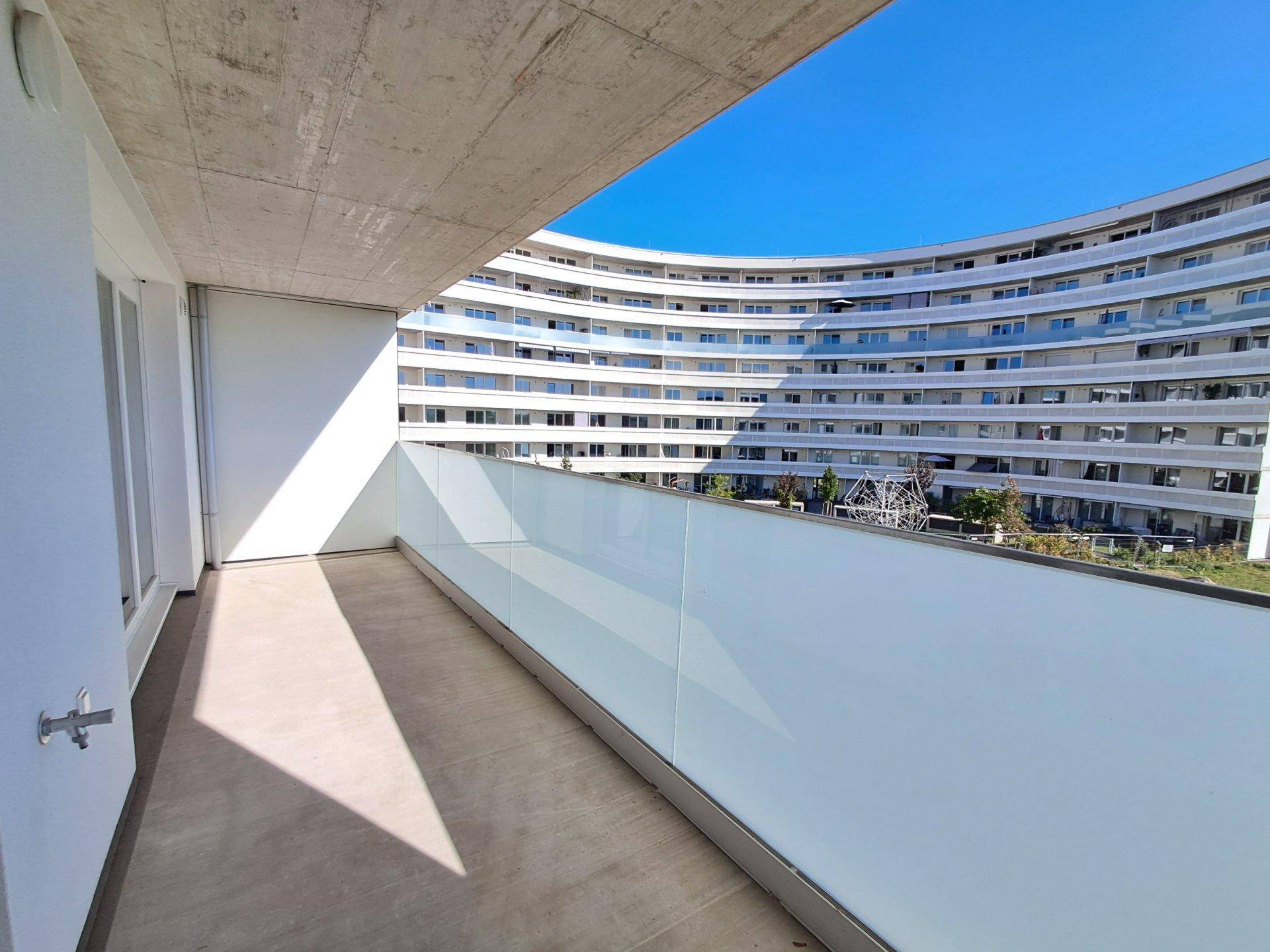 Geräumiger Balkon mit moderner Glasbrüstung und Blick auf ein weiteres Gebäude.