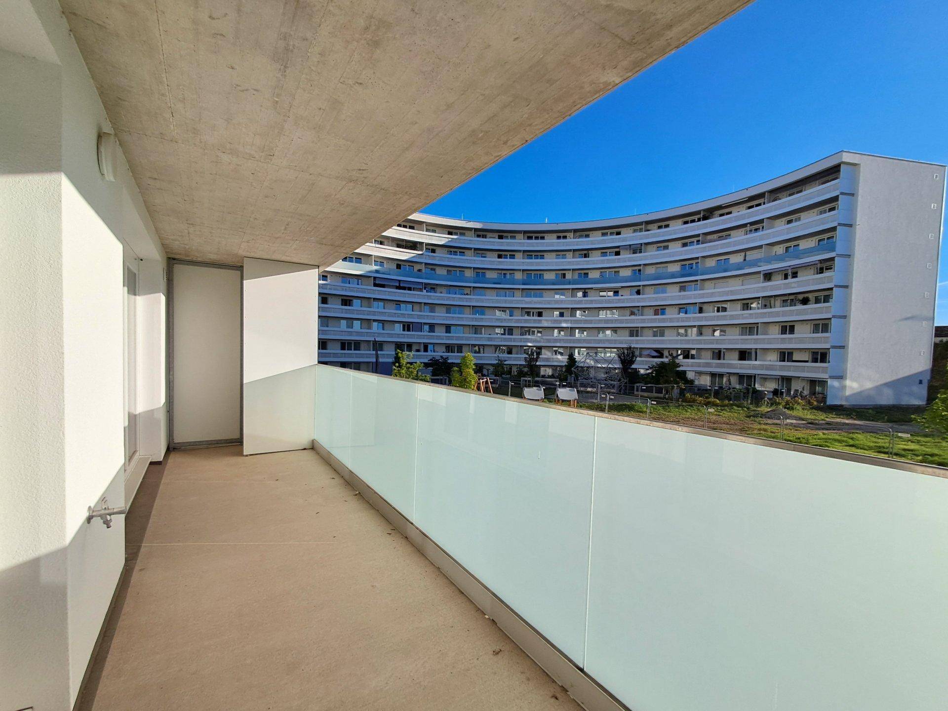 Geräumiger Balkon mit Blick auf ein weiteres modernes Wohngebäude unter blauem Himmel.