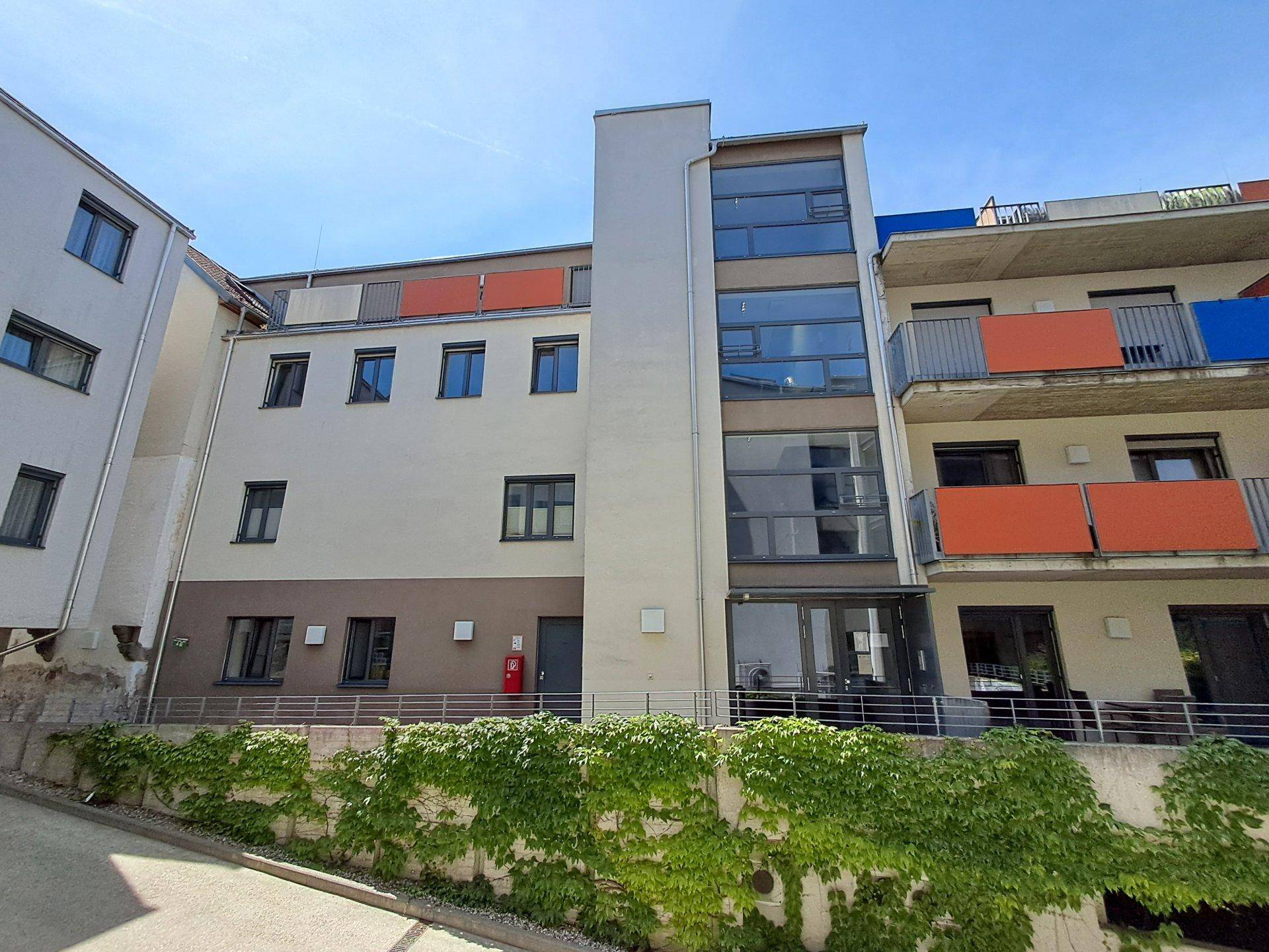 Moderne Wohnanlage mit heller Fassade, großen Fenstern und begrüntem Hangbereich.
