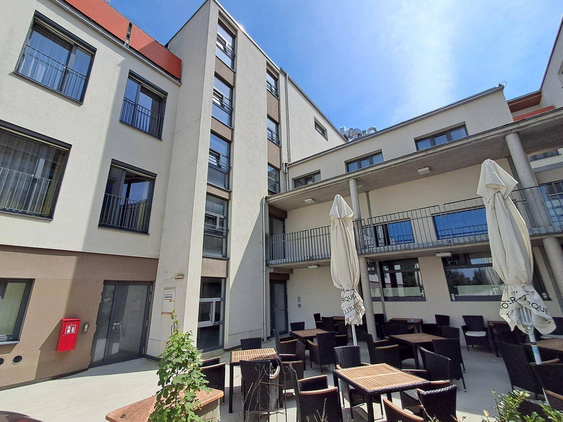 Möblierter Außenbereich mit Sonnenschirmen und Tischen in einem Innenhof der Wohnanlage.