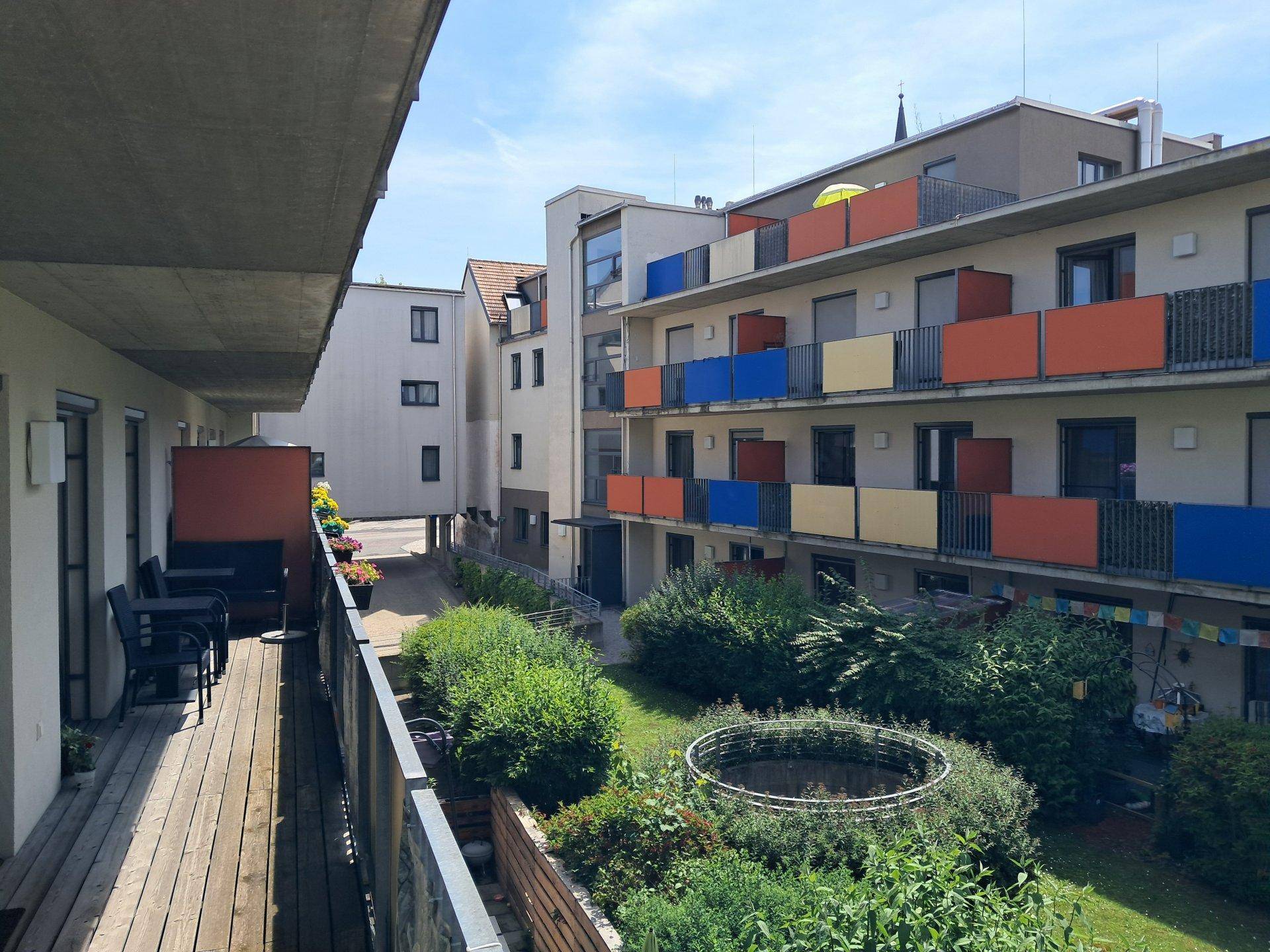 Balkon mit Holzboden und Blick auf den begrünten Innenhof der Wohnanlage.