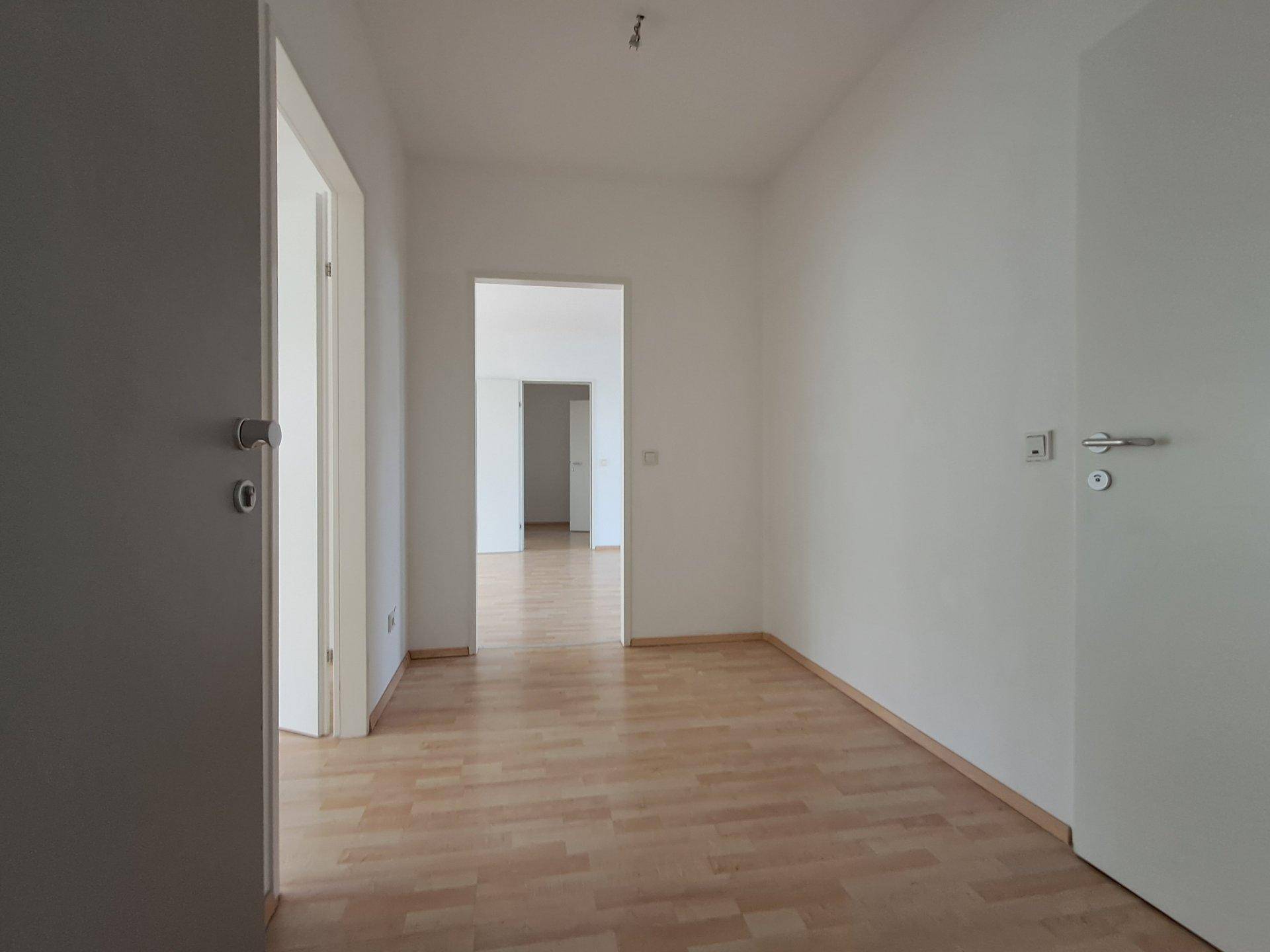 Heller Flur mit Laminatboden und weißen Wänden, der zu weiteren Räumen führt.