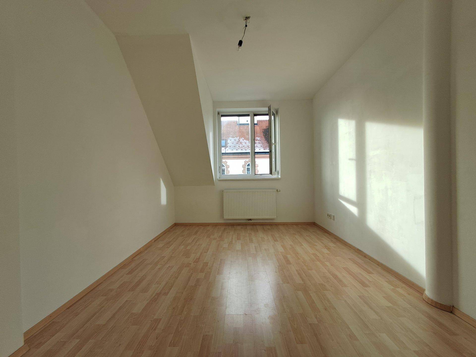 Heller Raum mit Laminatboden, weißen Wänden und Dachschräge, ideal als Schlafzimmer.