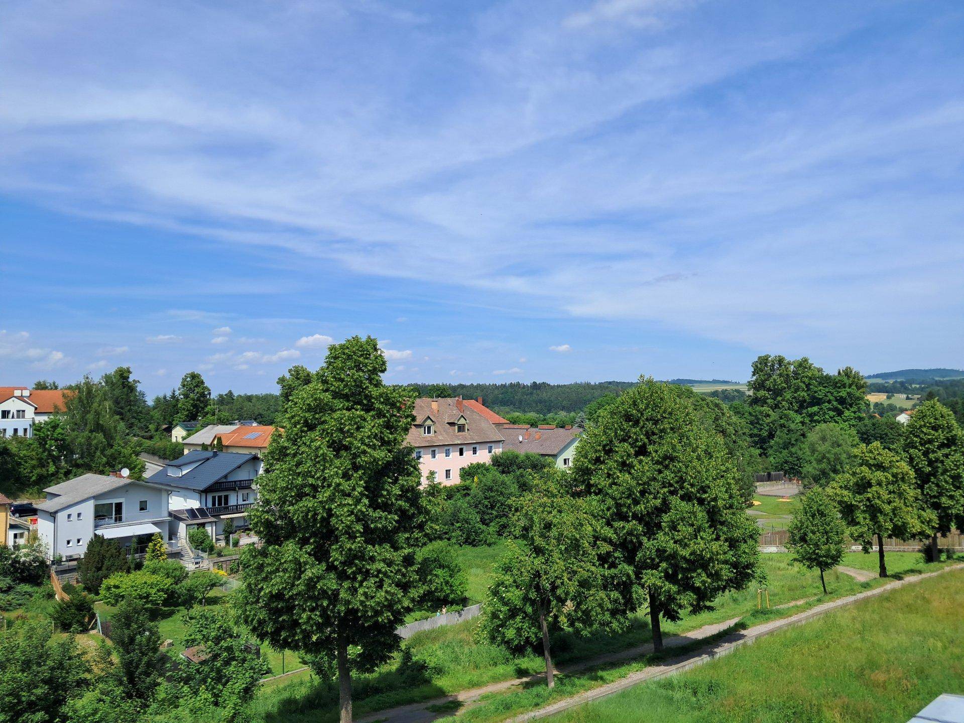 Weitläufiger Blick über eine grüne Landschaft mit vereinzelten Häusern und Bäumen.