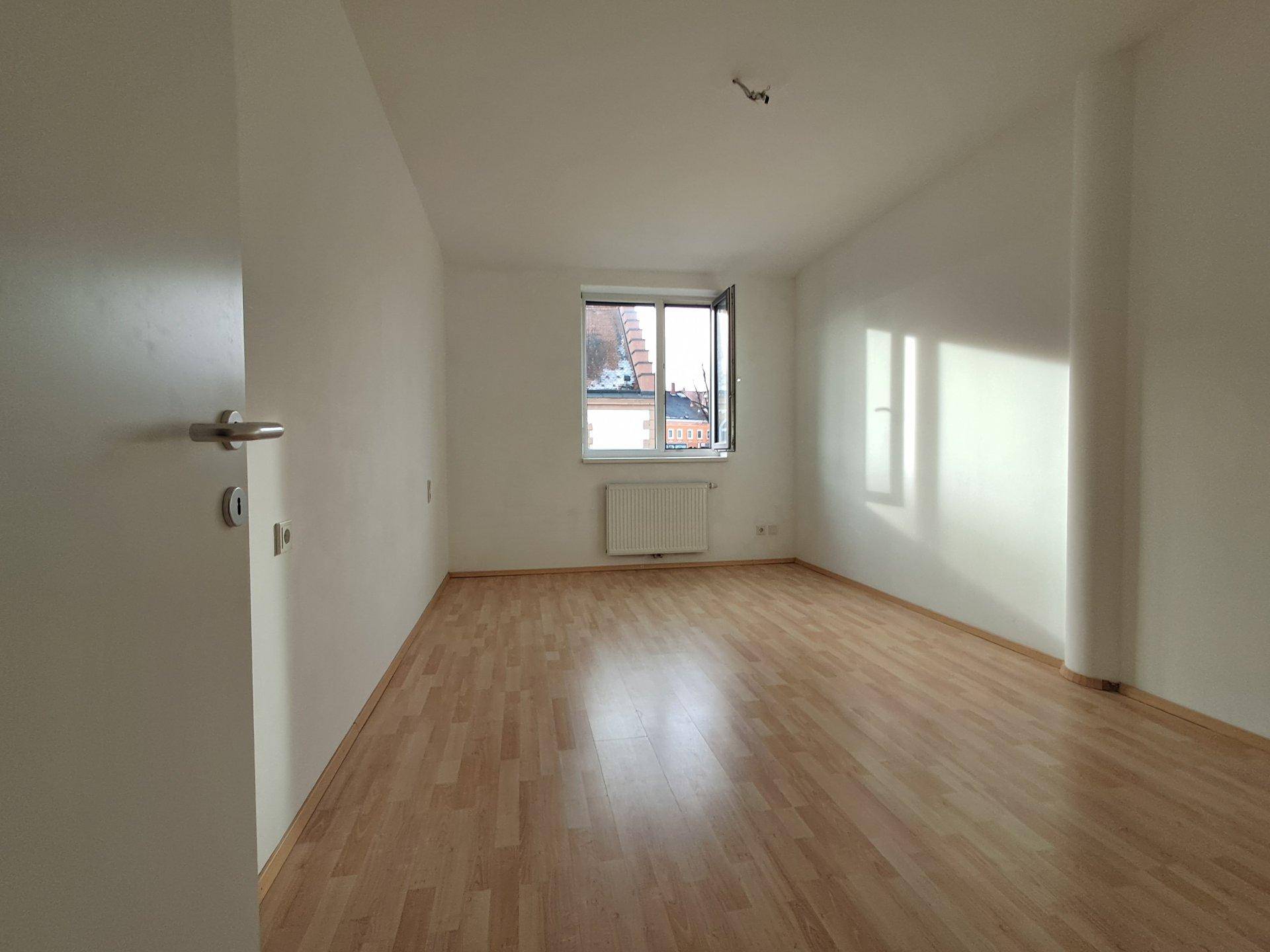 Heller Raum mit Laminatboden, weißen Wänden und Dachschräge, gut belichtet durch das Fenster.