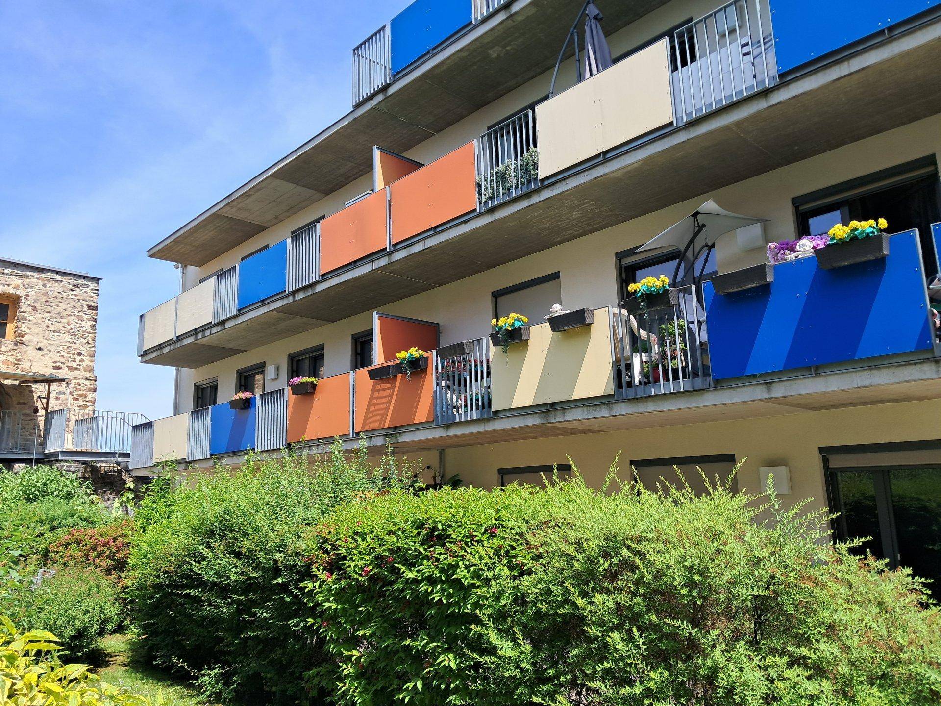 Mehrstöckiges Wohngebäude mit farbigen Balkonen und üppiger Bepflanzung im Vordergrund.