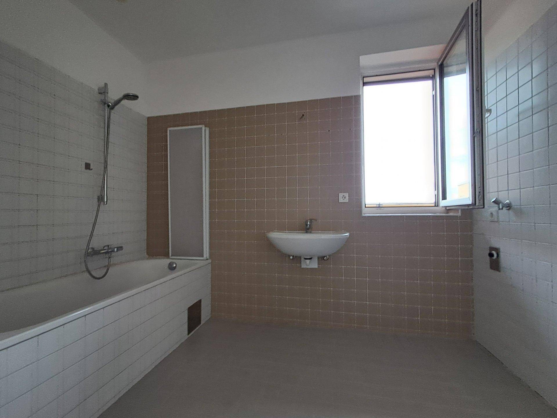 Badezimmer mit Badewanne, Waschbecken und Fenster, gefliest in Braun- und Weißtönen.