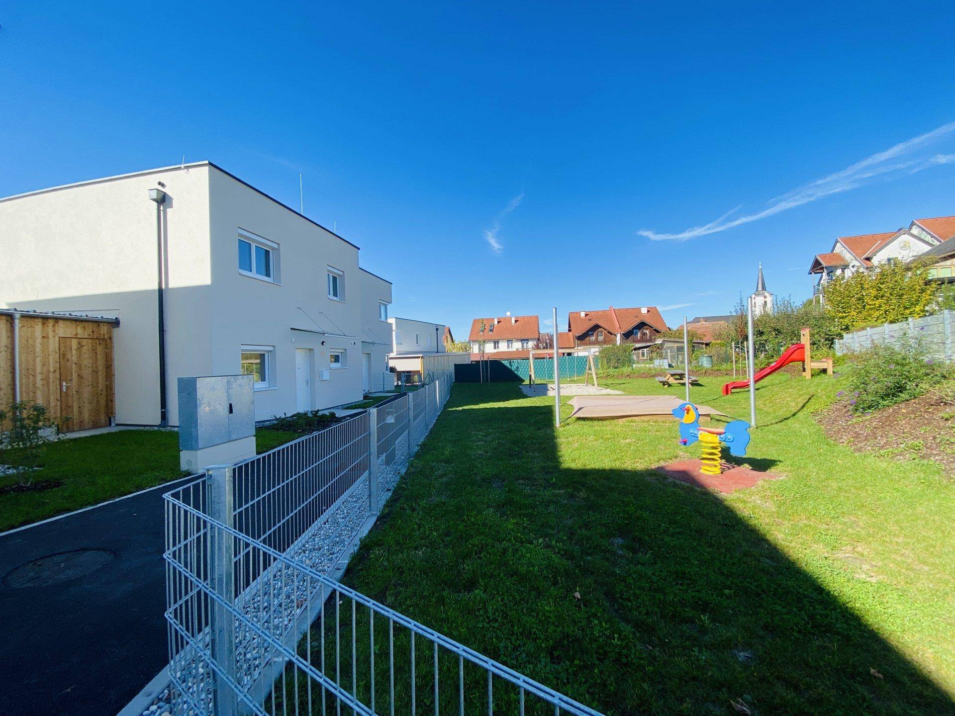 Reihenhaus mit angrenzendem Spielplatz, Rasenfläche und Blick auf die ländliche Umgebung.