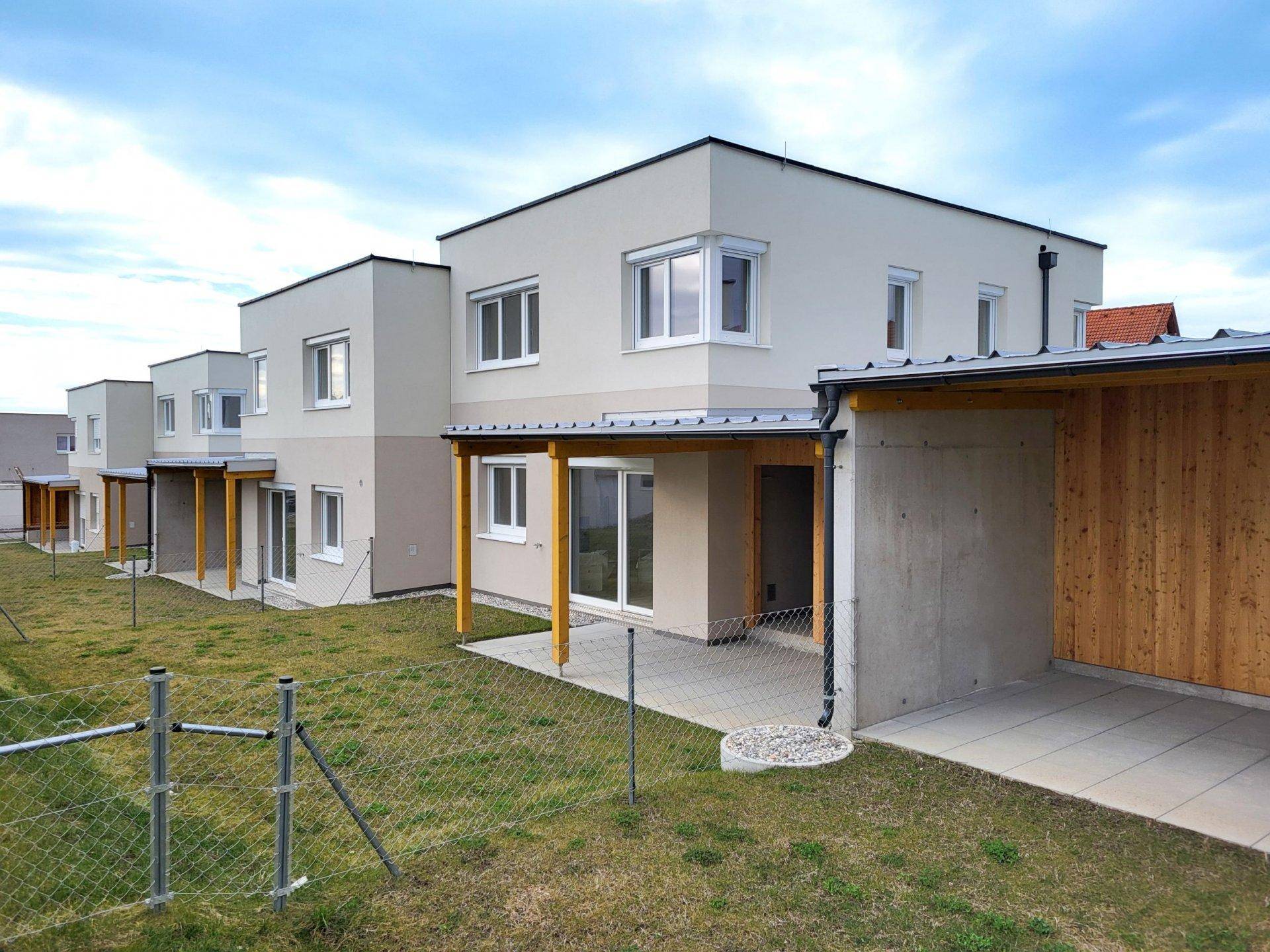 Rückseite der Reihenhäuser mit überdachter Terrasse, Gartenbereich und angrenzendem Carport.