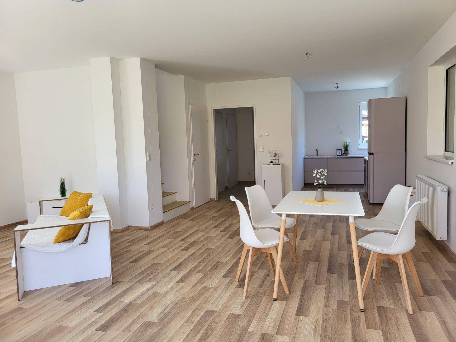 Heller offener Wohn- und Essbereich mit Laminatboden und moderner, minimalistischer Einrichtung.