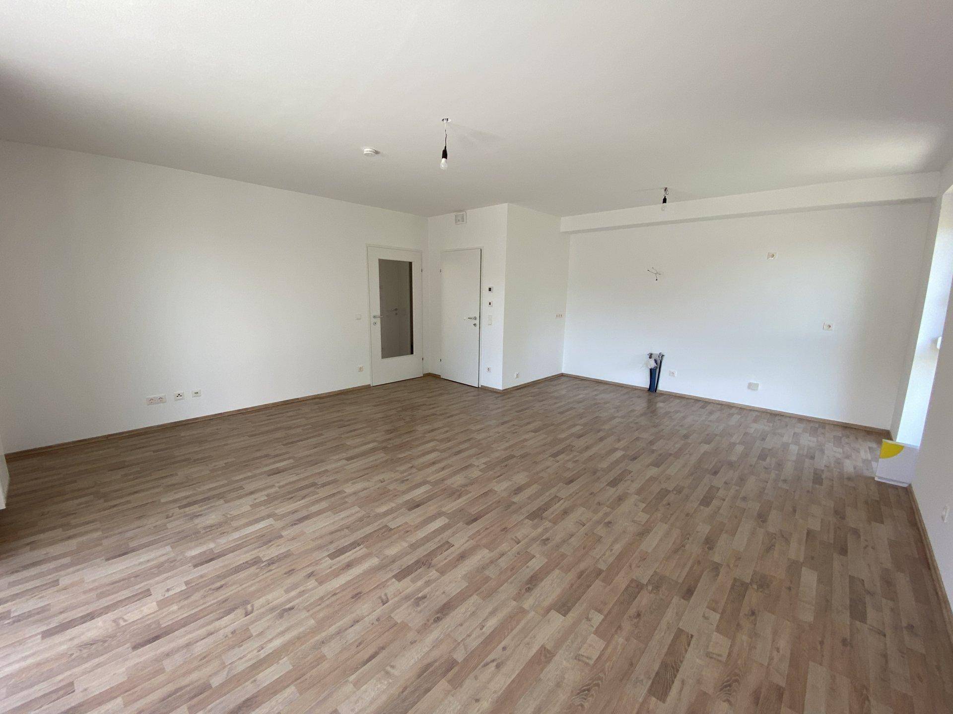 Geräumiger Wohnbereich mit Laminatboden und Anschlüssen für eine zukünftige offene Küche.