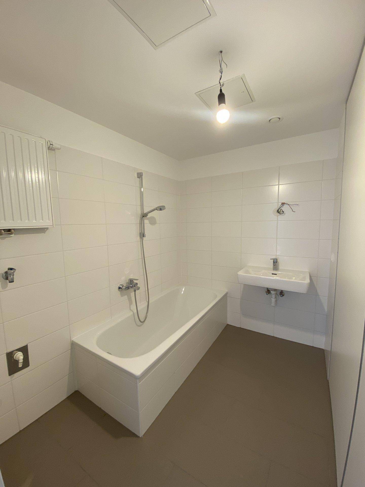 Modernes Badezimmer mit Badewanne, Waschbecken und weißen Fliesen, funktional und hell gestaltet.