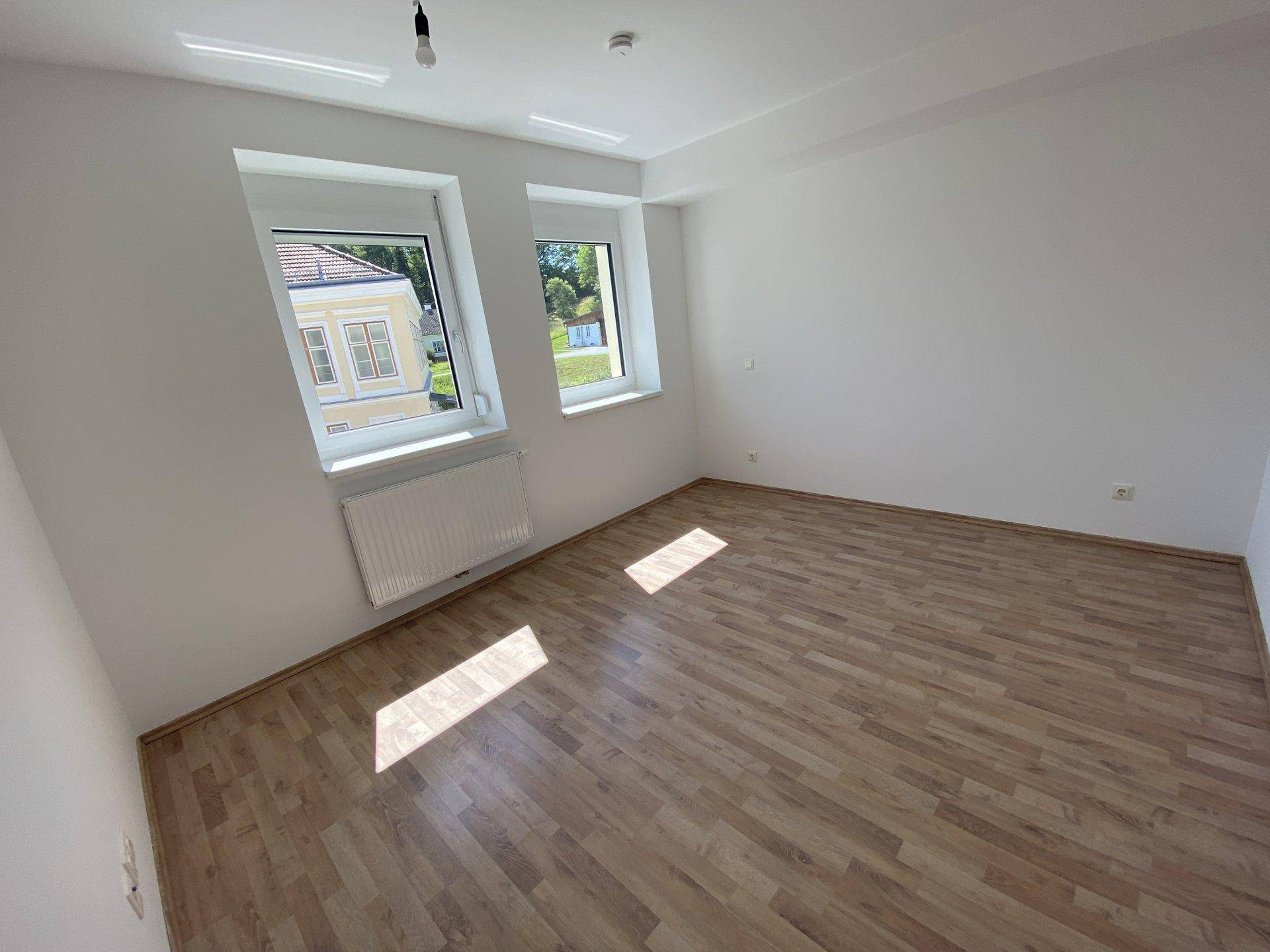 Sonniges Schlafzimmer mit Laminatboden und Blick ins Grüne, ideal für erholsame Nächte.