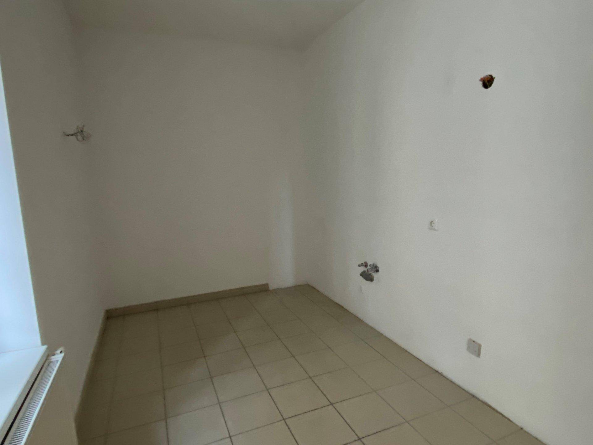 Leerer Raum mit Fliesenboden und Anschlüssen für eine Küche, bereit zum Einbau.