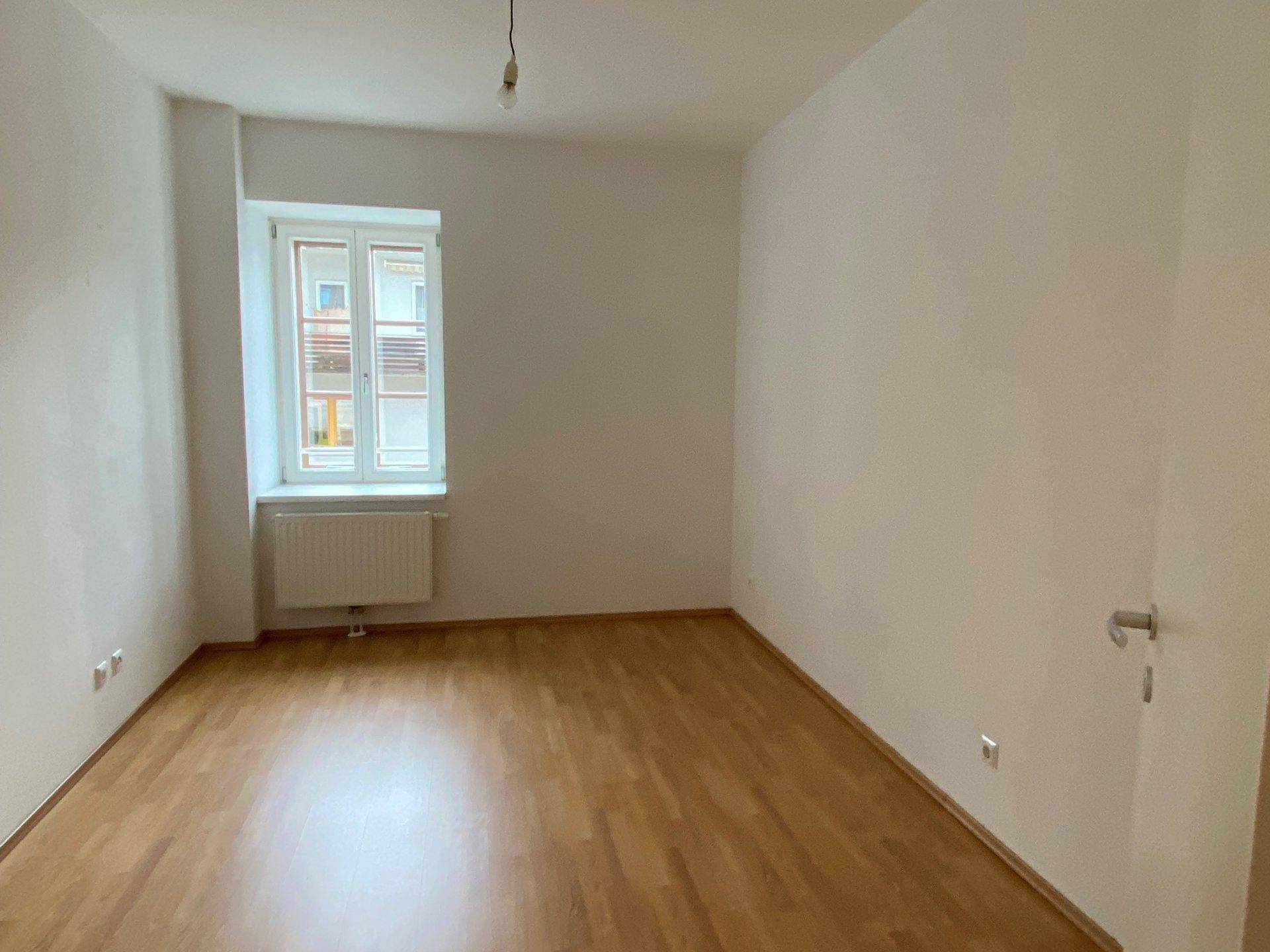 Leeres Zimmer mit Holzfußboden und einem Fenster, ideal als Schlafzimmer oder Arbeitszimmer.