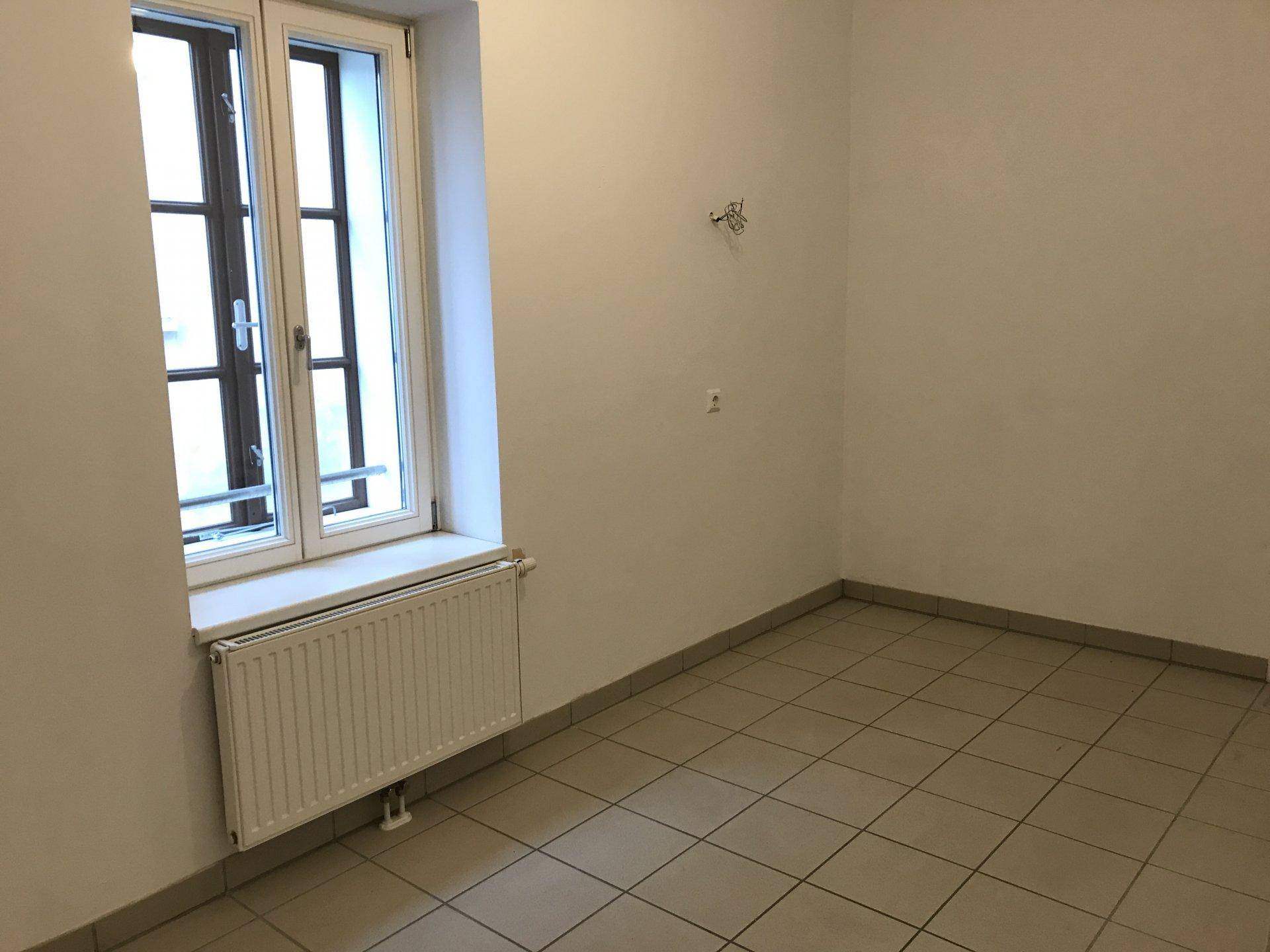 Leerer Raum mit Fliesenboden und einem Fenster, geeignet für eine Küche oder einen Abstellraum.