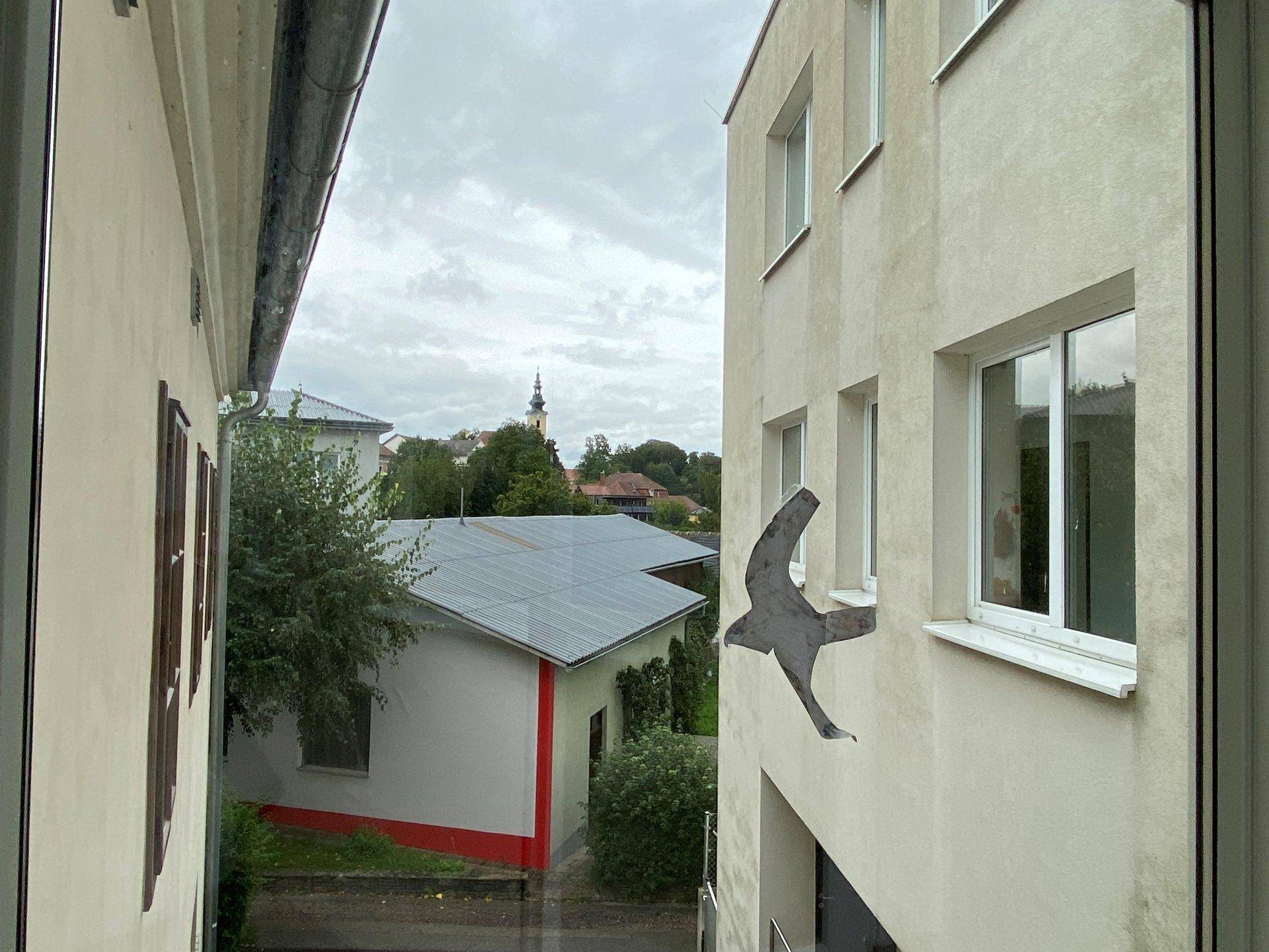 Blick aus dem Fenster auf ein Nachbargebäude und einen Kirchturm in der Ferne.