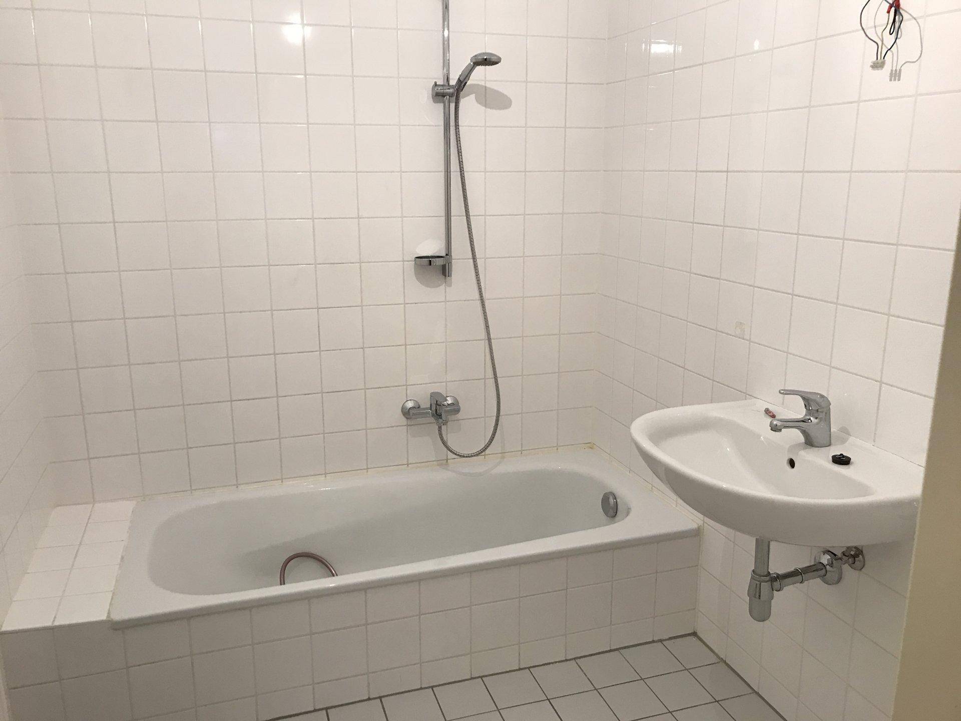 Badezimmer mit weiß gefliesten Wänden, Badewanne mit Duschfunktion und einem Waschbecken.