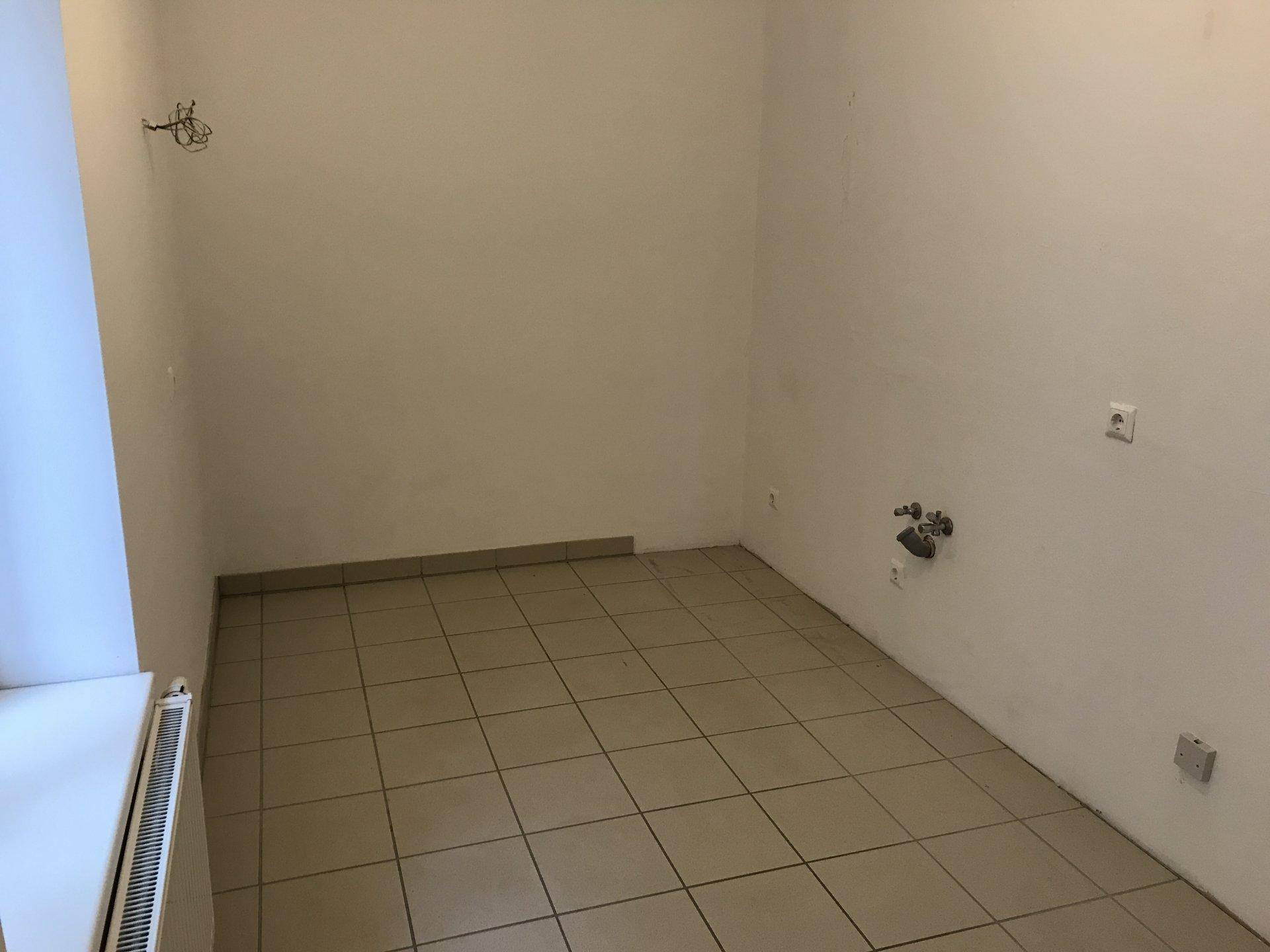 Leerer Raum mit Fliesenboden und Anschlüssen für eine Küche, bereit zum Einbau.