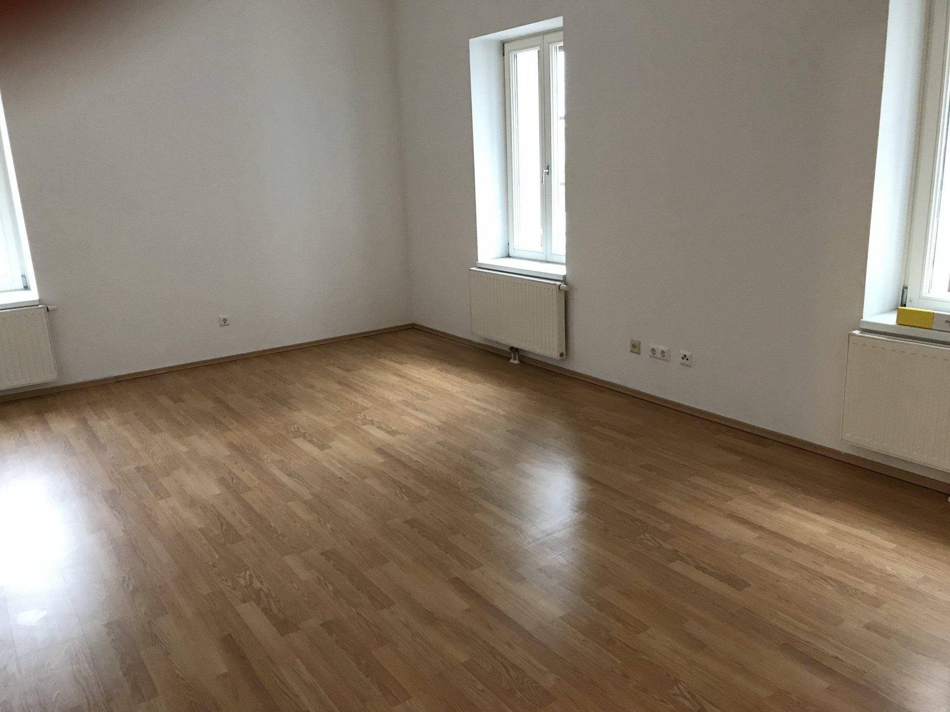 Helles, geräumiges Zimmer mit Parkettboden und zwei Fenstern, ideal als Wohnbereich.