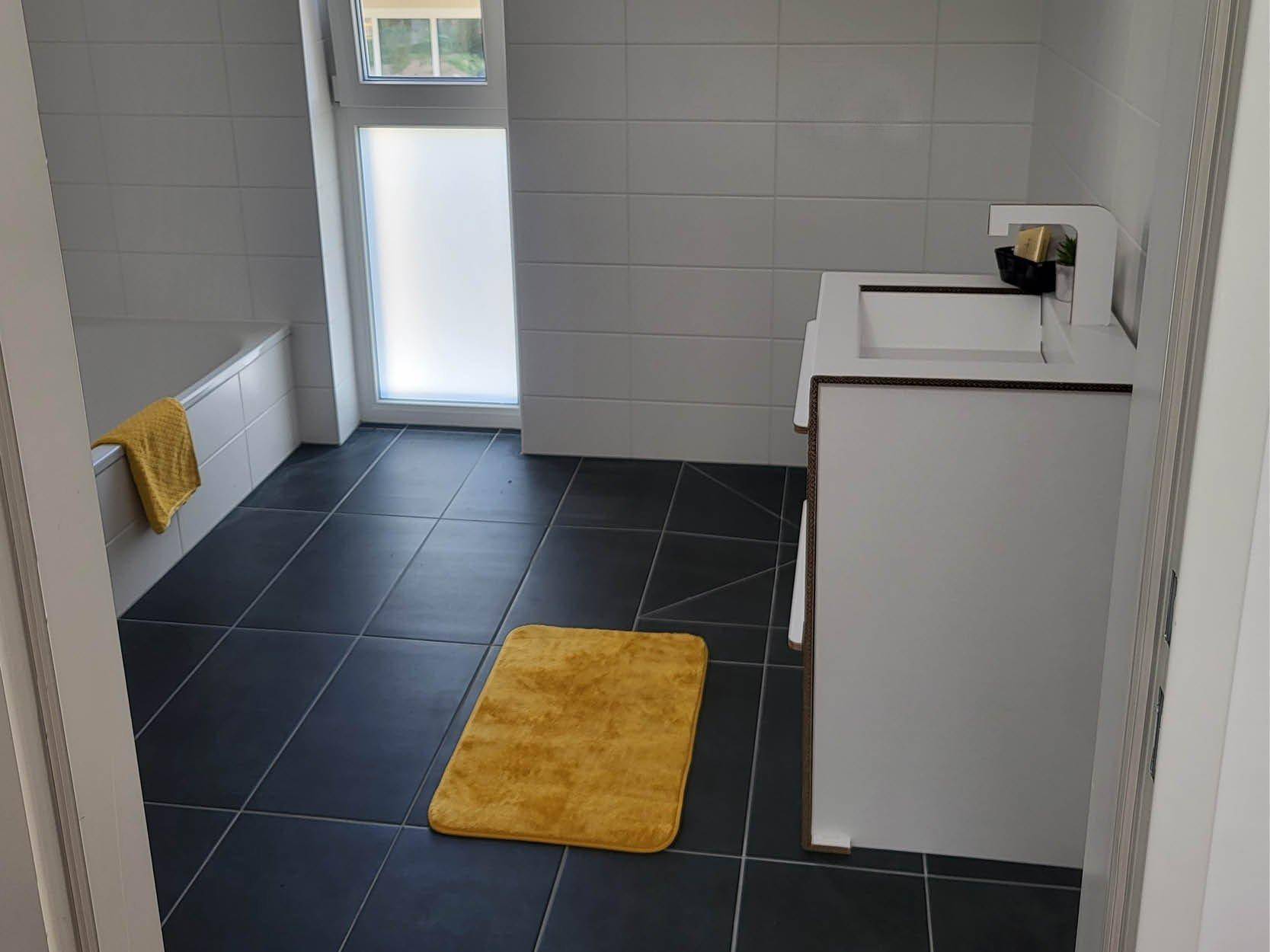 Modernes Badezimmer mit dunklen Fliesen, Badewanne und Fenster für Tageslicht.
